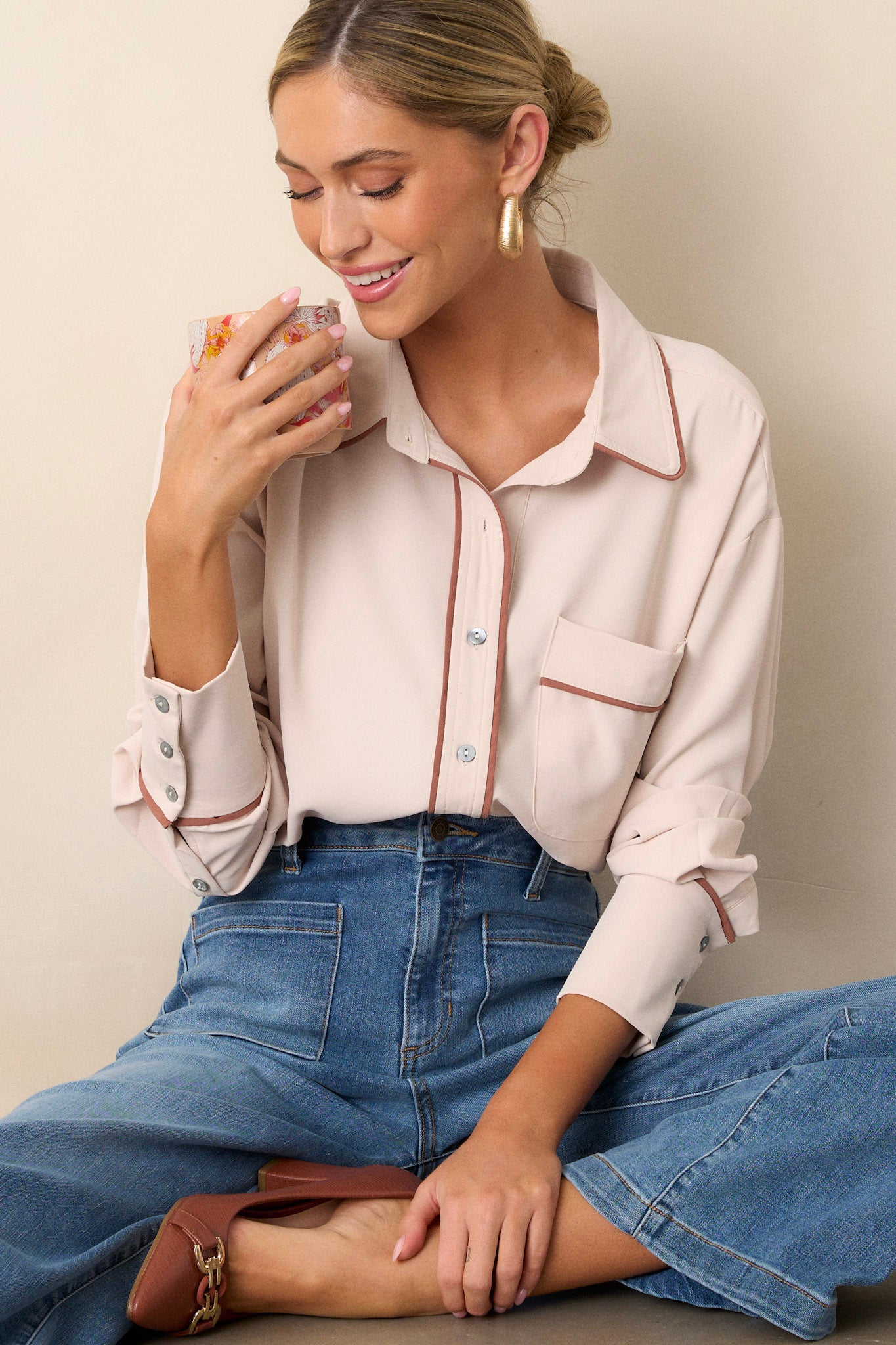 This beige top features a collared neckline, a functional breast pocket, a full button front, contrasting trim, and button cuffed long sleeves.