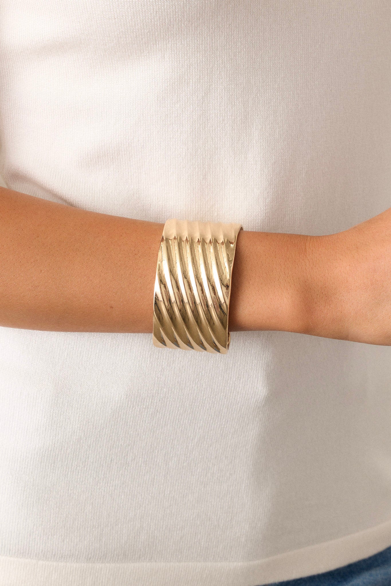 This gold cuff features shiny hardware, a textured material, a thick band, and rounded edges.