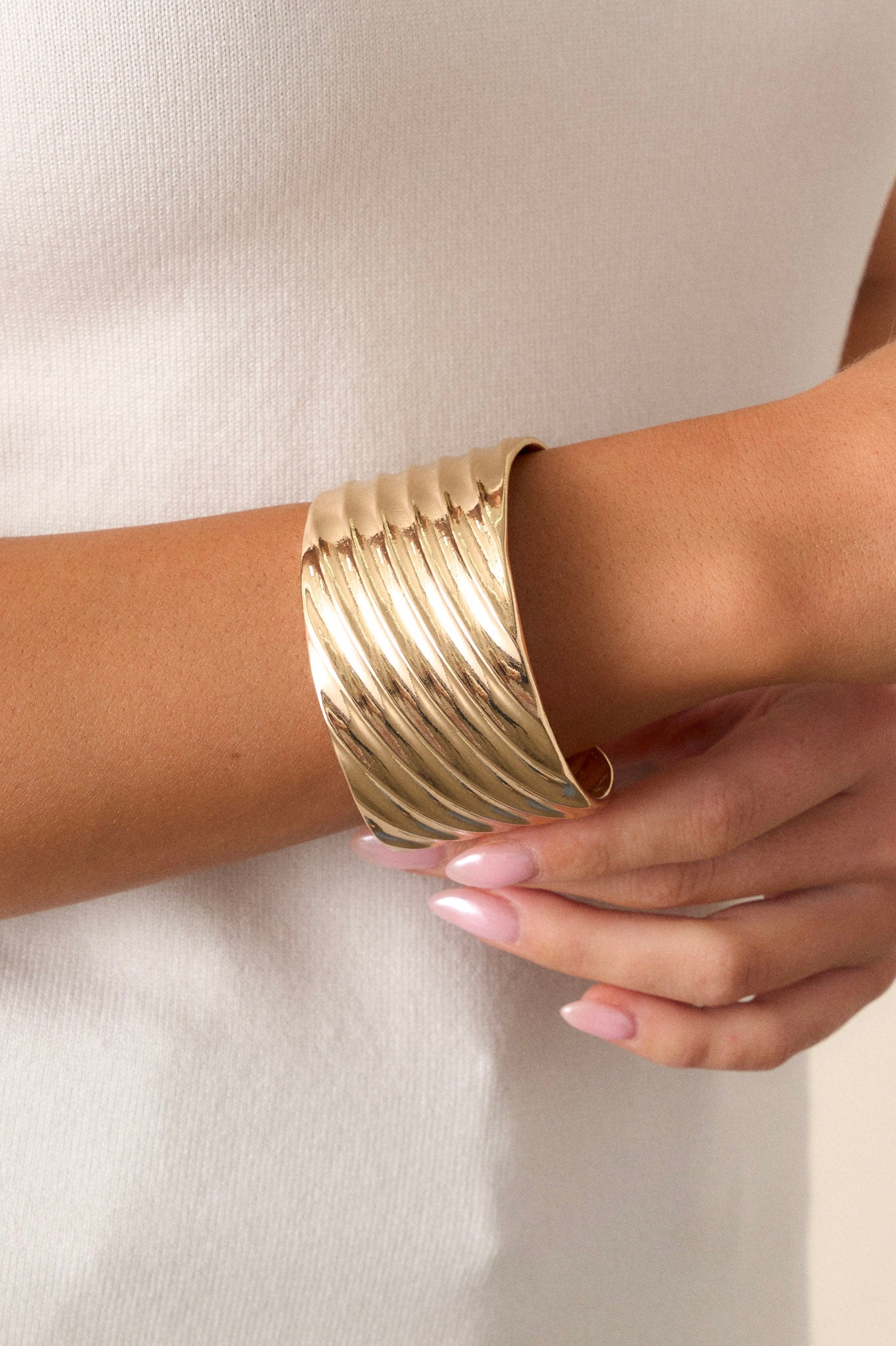 Close-up view of this gold cuff that features shiny hardware, a textured material, a thick band, and rounded edges.