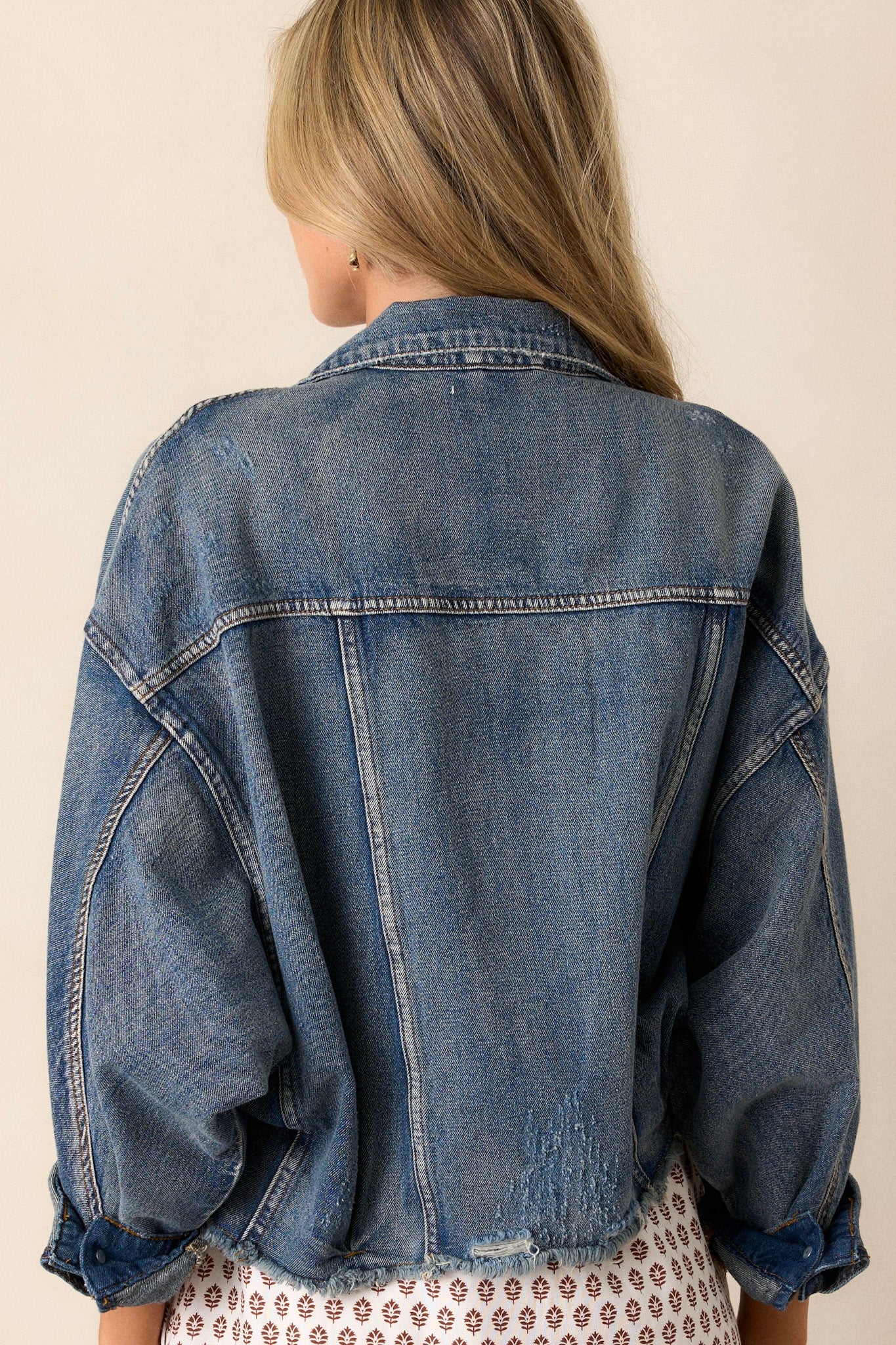 Back view of a denim jacket highlighting the distressed details, prominent dolman sleeves, and the overall structure of the back panel.