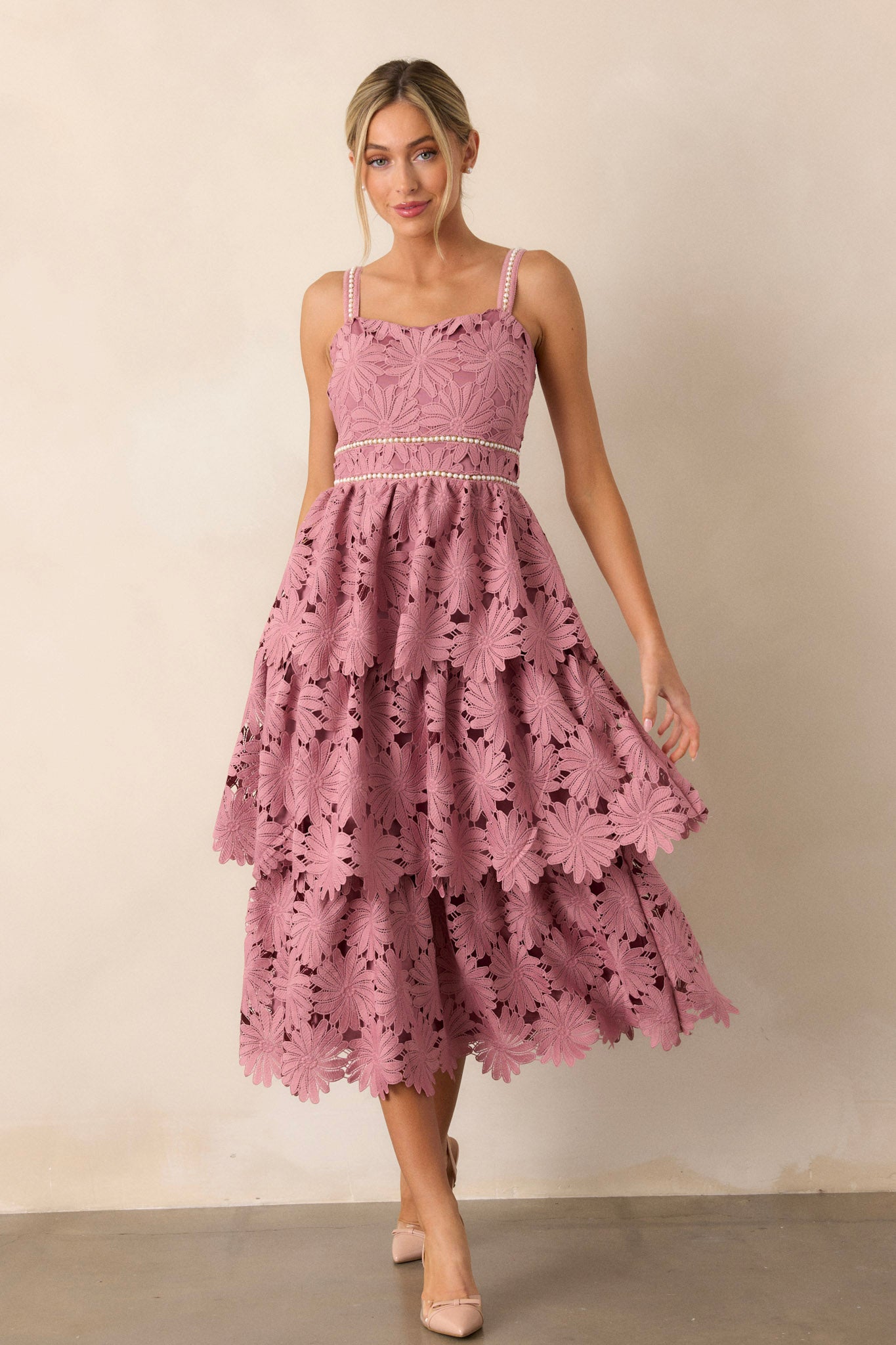 Front angled view of the dusty pink dress featuring a square neckline, faux pearl decorated waistline, lace tiered design, and faux pearl decorated spaghetti straps