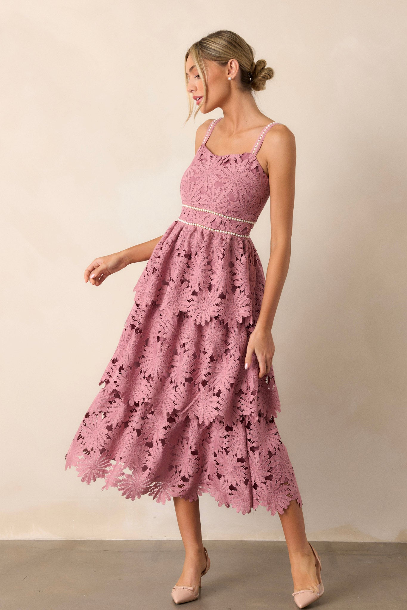 Front view of a dusty pink dress featuring a square neckline, a faux pearl decorated waistline, a lace tiered design, a discrete back zipper, and faux pearl decorated spaghetti straps