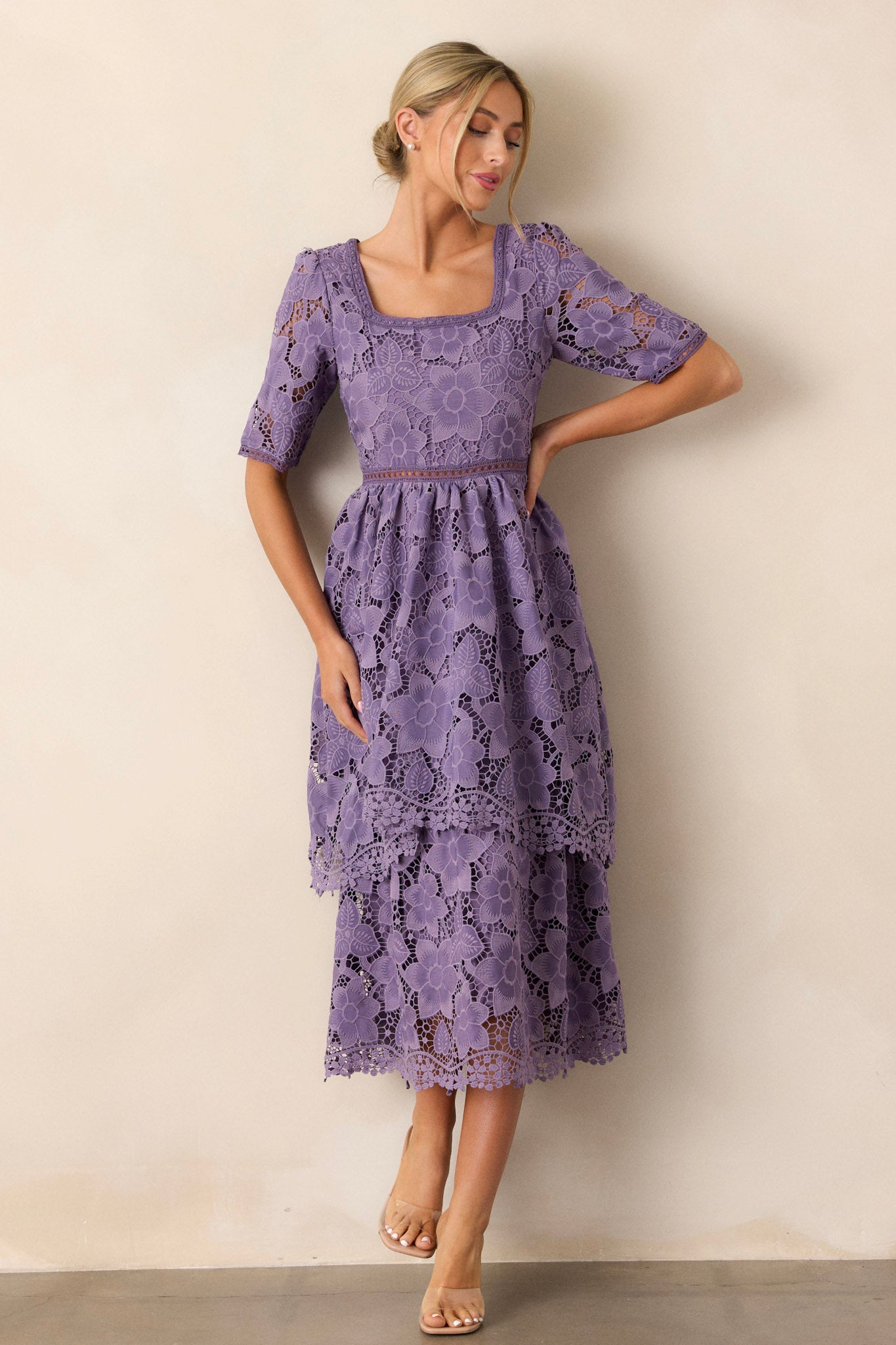 Front view of a lilac dress featuring a square neckline, a lace floral design, a lace cutout waist design, a tiered skirt, and half sleeves.