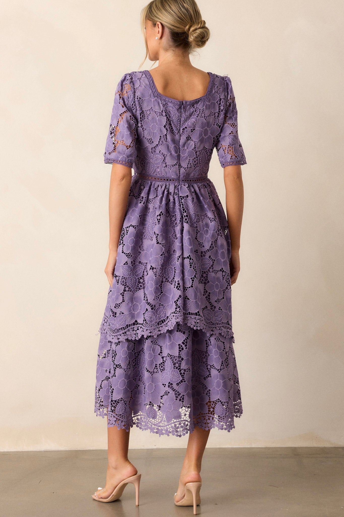 Back view of the lilac dress highlighting the discrete back zipper, the continuation of the lace floral design, and the tiered skirt.