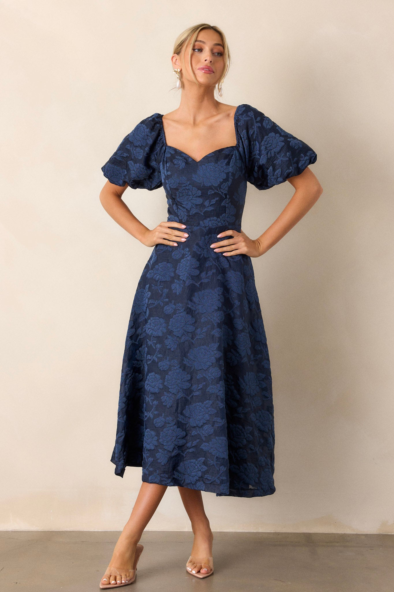 Full-length view of a model wearing the navy floral dress, emphasizing the Queen Anne neckline, fitted bodice, floral design, and the elastic cuffed puff sleeves