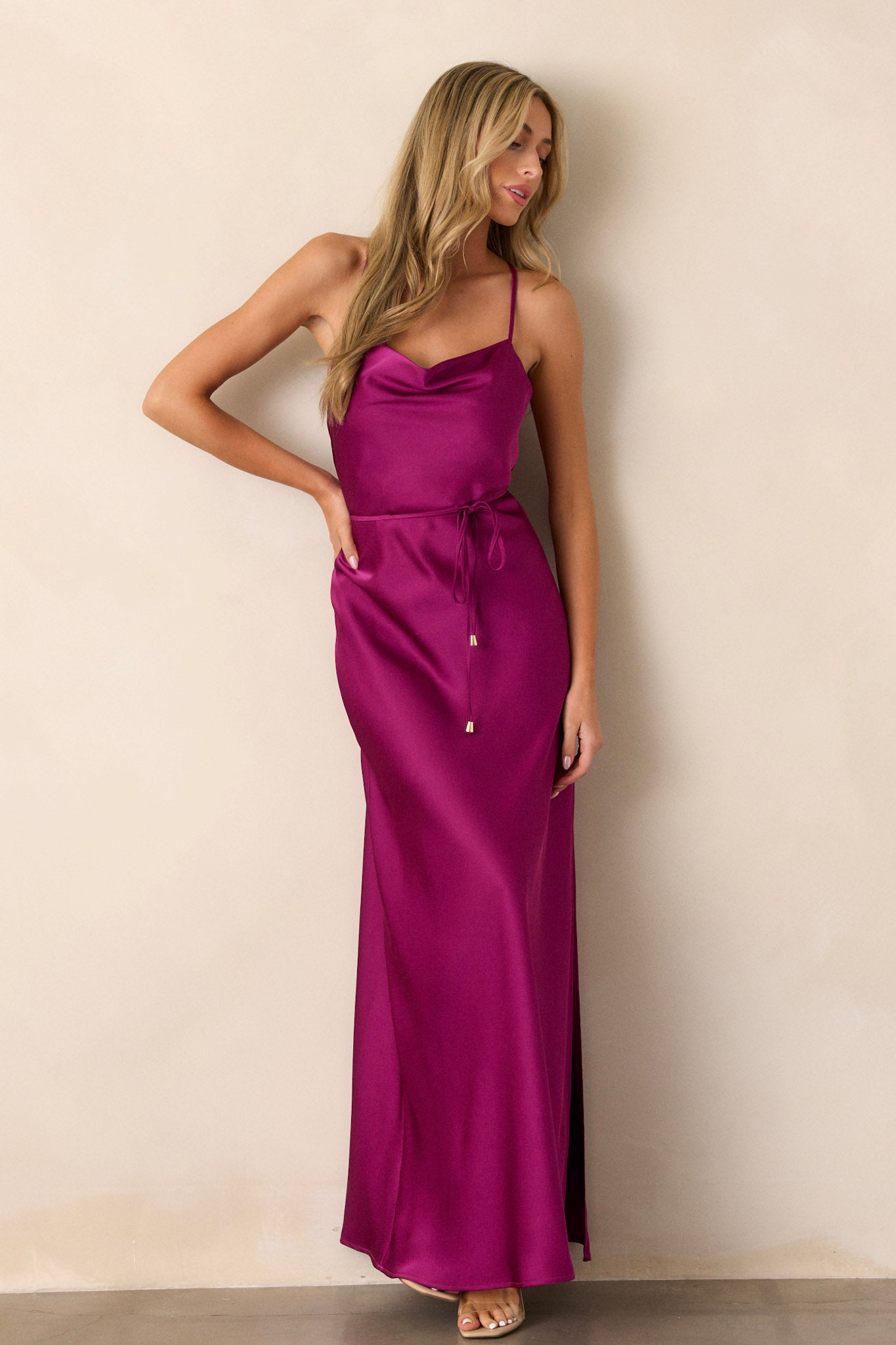 Side view of the magenta dress showcasing the cowl neckline, adjustable straps, the self-tie belt with gold hardware, and the left-side slit reaching knee length.