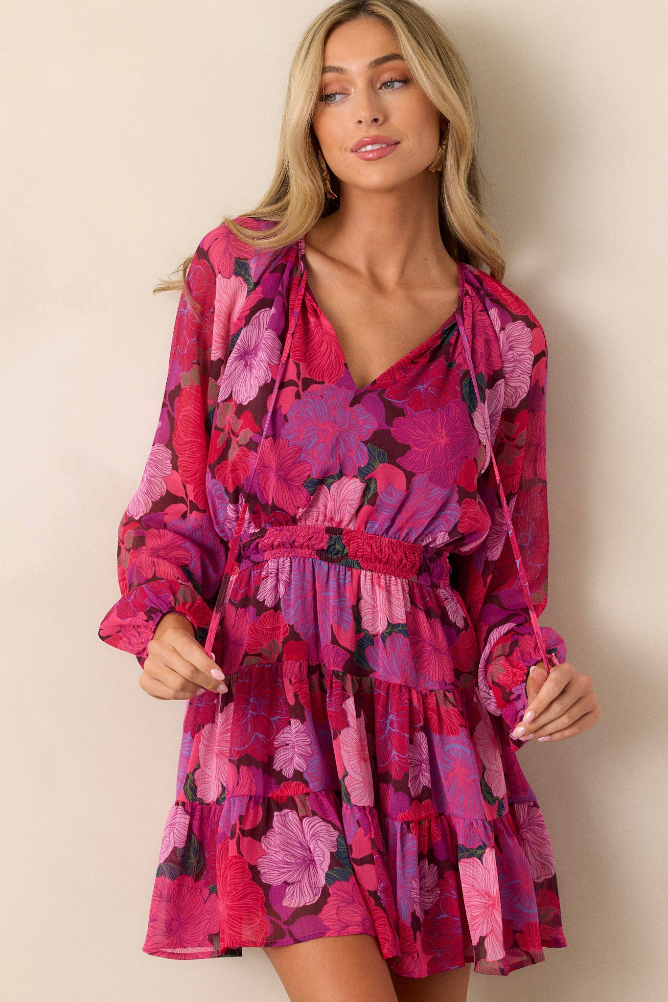 Front view of a pink dress featuring a v-neckline, flowy and breezy sleeves, a tie front detail, and a smocked waistband