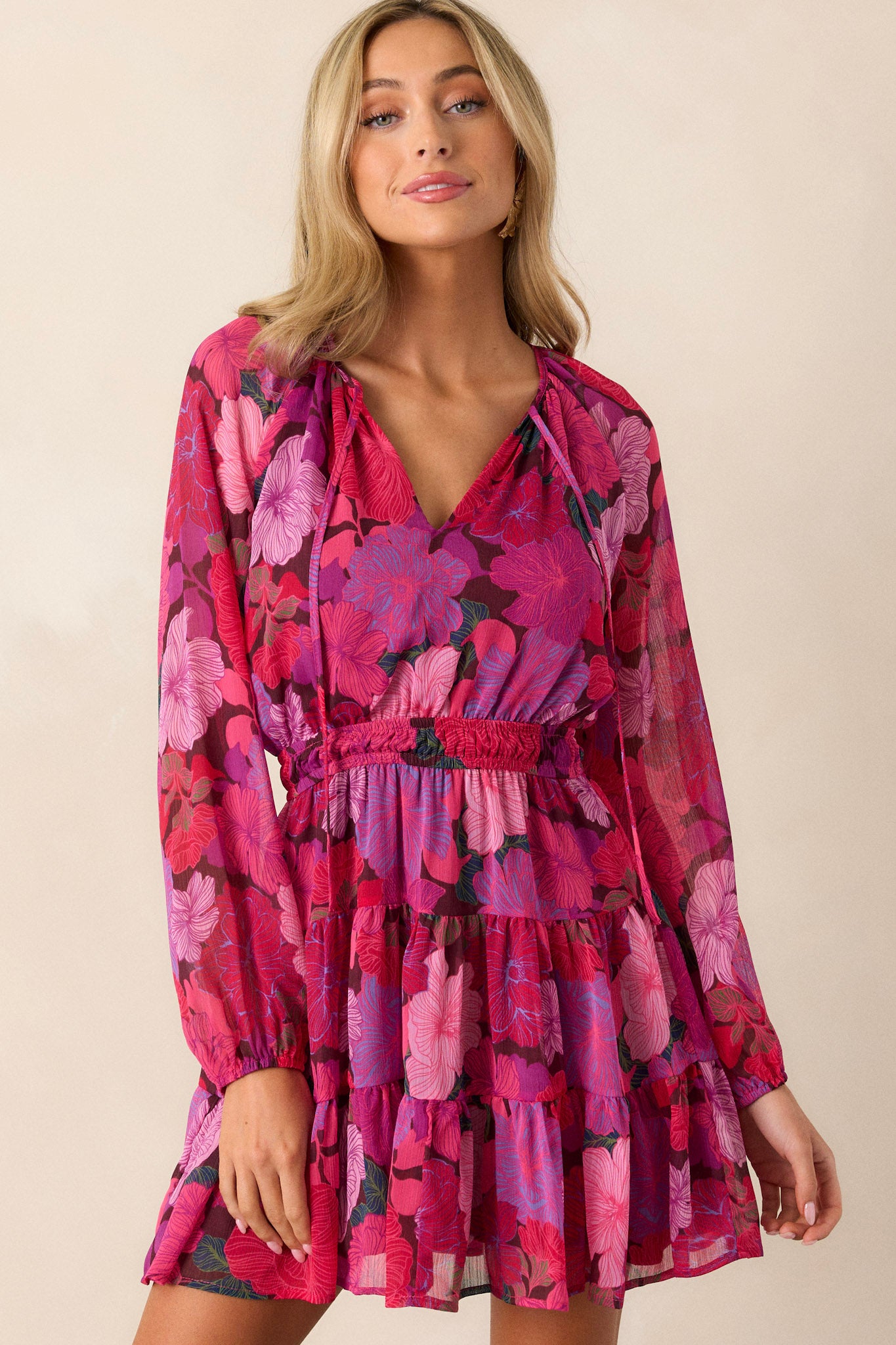 Front angled view of the pink dress featuring a v-neckline, flowy and breezy sleeves, a tie front detail, and a smocked waistband