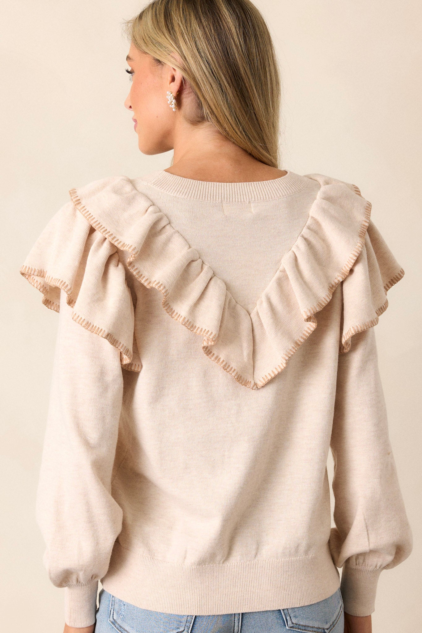 Back view of the beige top highlighting the high neckline, the back design, and the ribbed hemline, with the ruffle detailing on the long sleeves visible