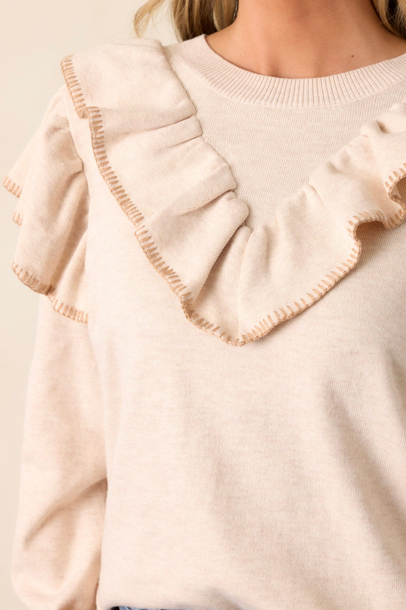 Close-up of the beige top focusing on the ruffle detail across the shoulders and chest, the ribbed hemline, and the ruffle detailing on the cuffed long sleeves.