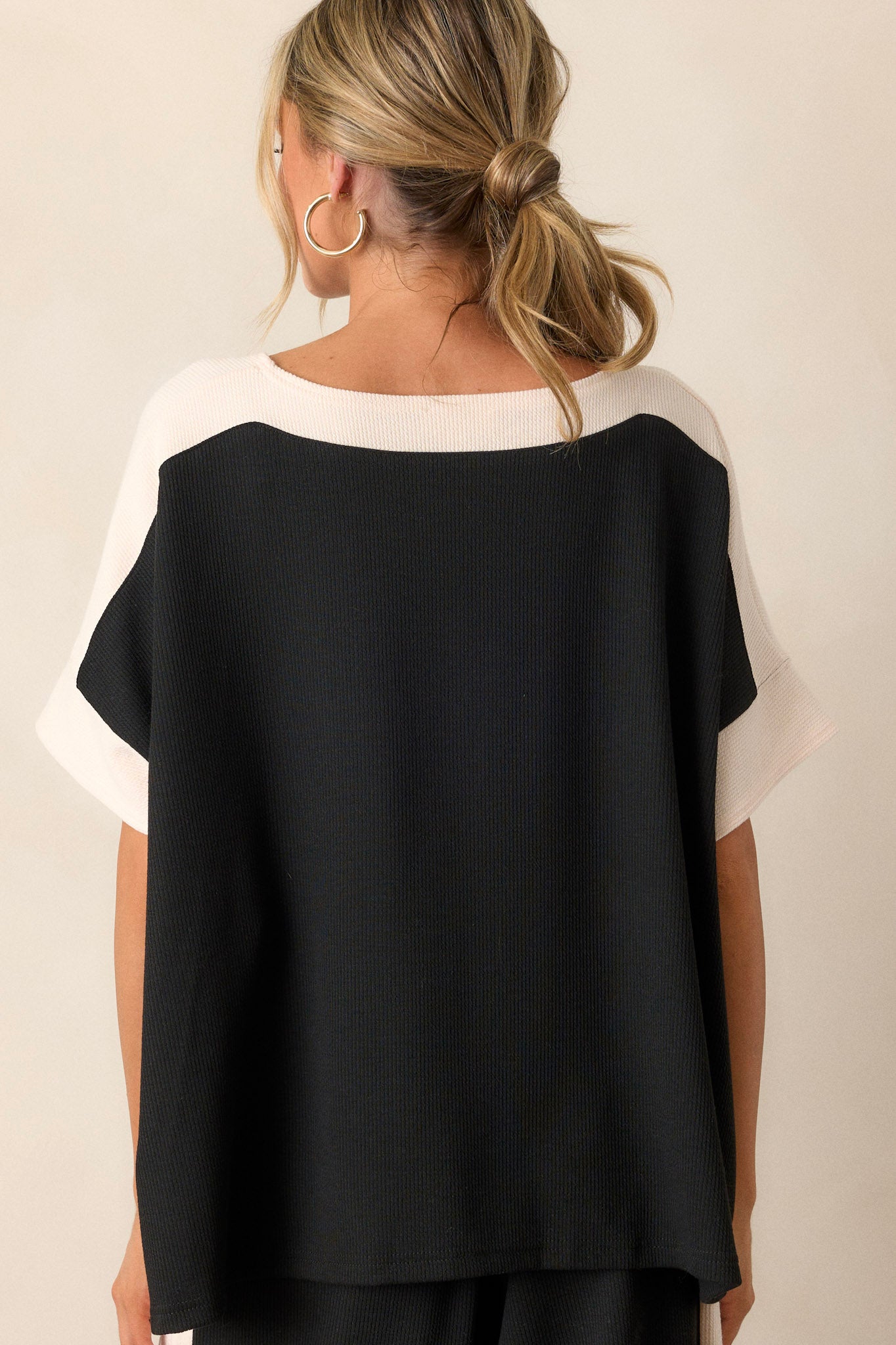 Back view of the black and ivory top highlighting the continuous ivory trim on the neckline and sides, along with the relaxed fit and slight ribbed texture