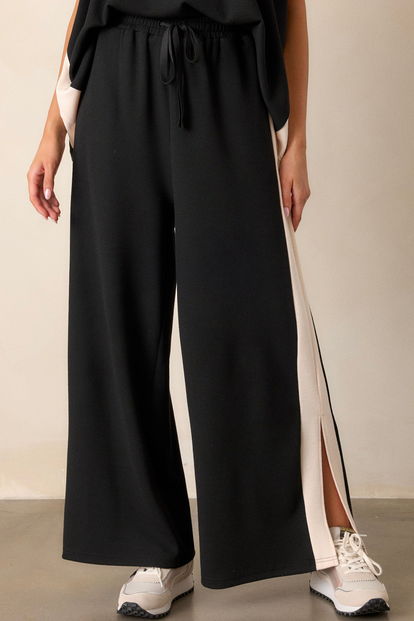 Angled view of the black and ivory pants displaying the high waisted design, the white trim along the legs, the soft ribbed texture, and the dramatic high slits that enhance the pants' movement.