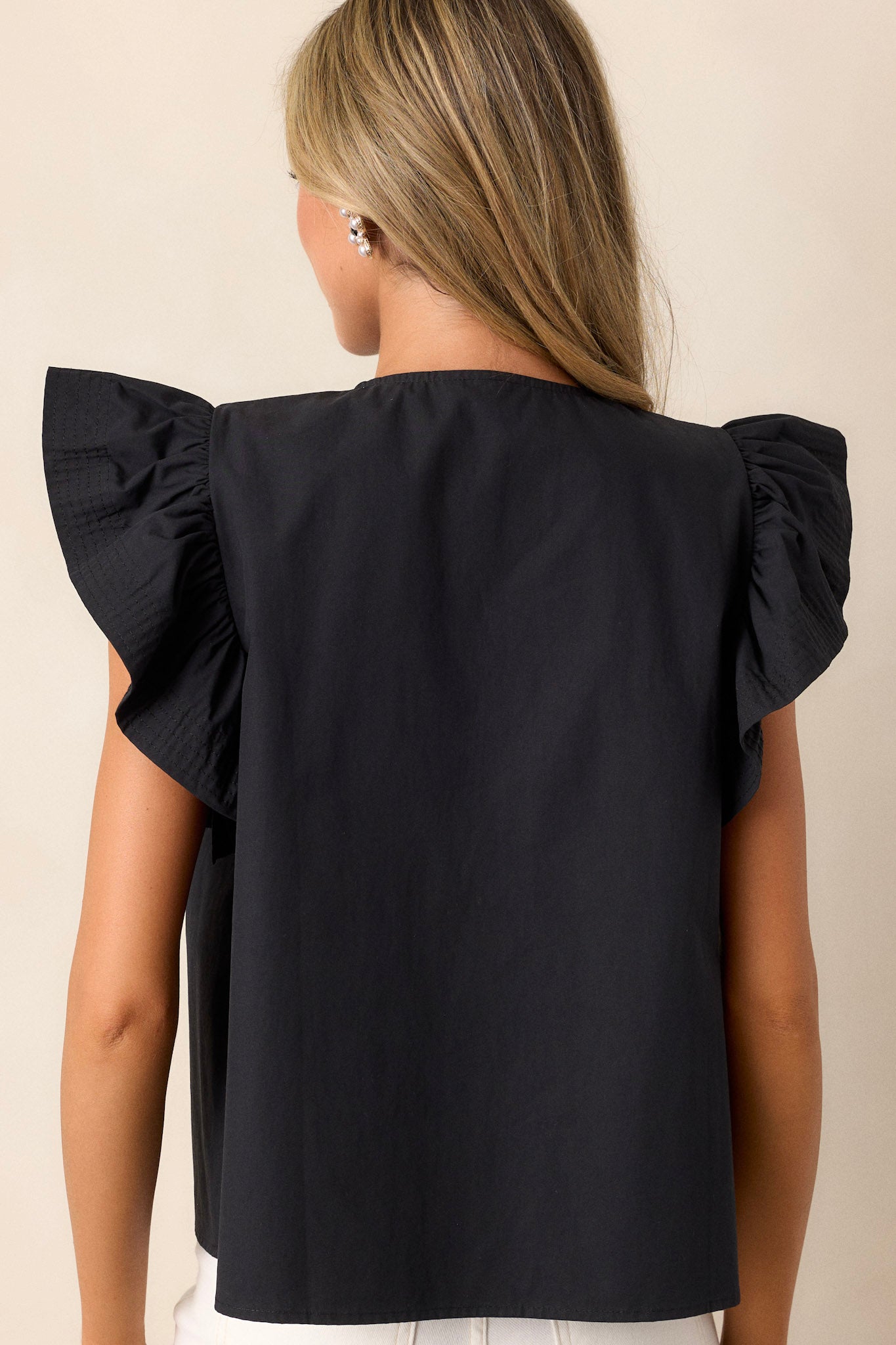 Back view of this black top that features a split neckline, pleated detailing on the shoulders, and short flutter sleeves.