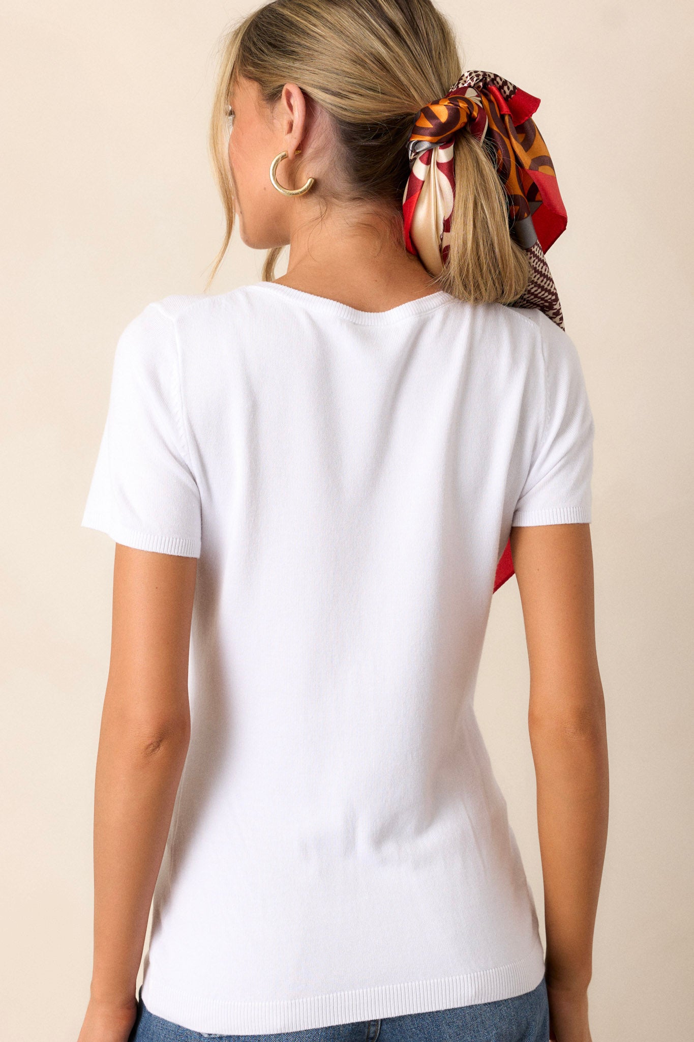 Back view of the white sweater top highlighting the ribbed hem and the soft texture of the fabric, along with the short sleeves.