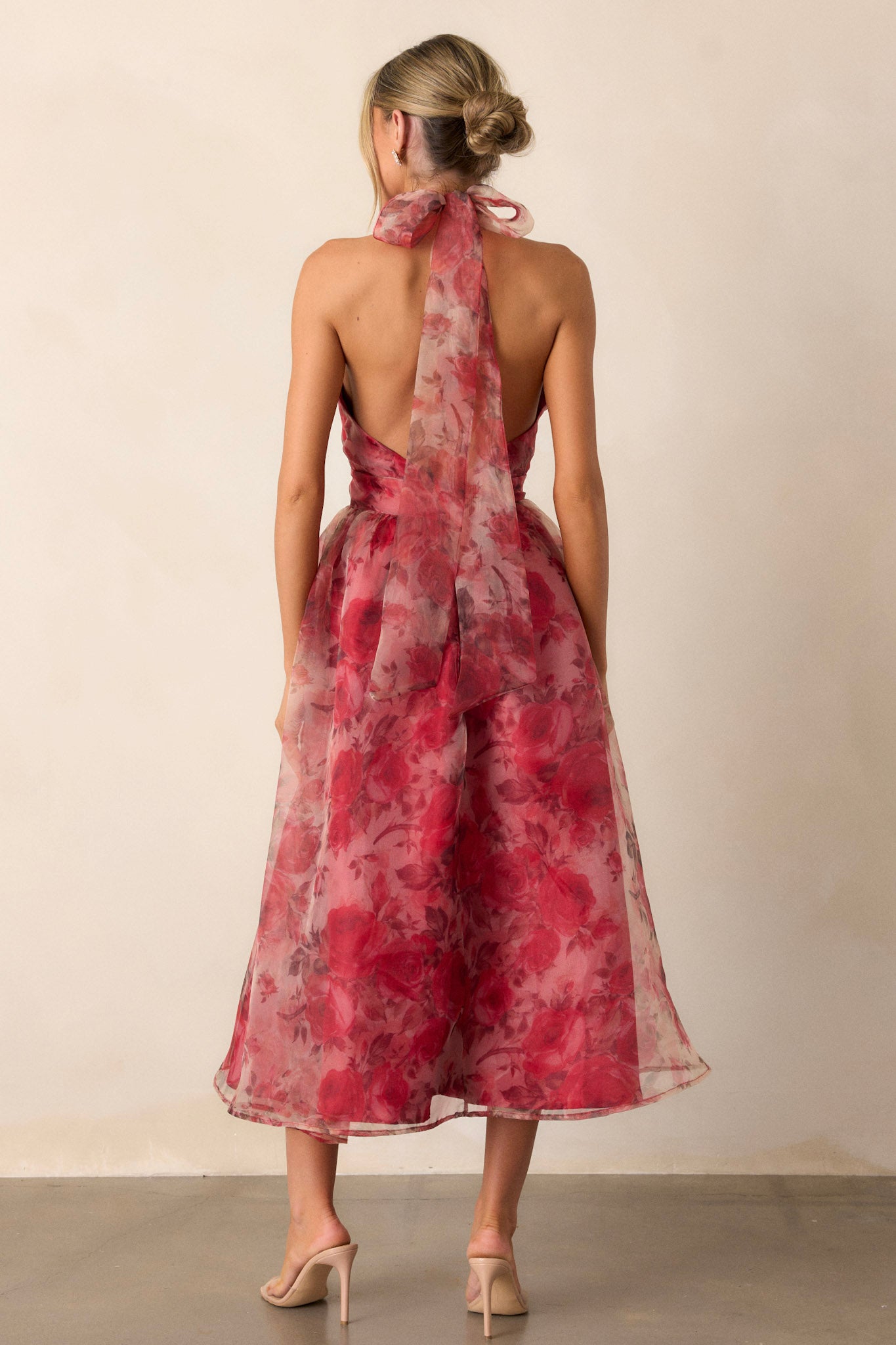 Back view of the red floral dress highlighting the low back design, with the halter-neck strap visible at the top, and the floral mesh pattern continuing down the back.