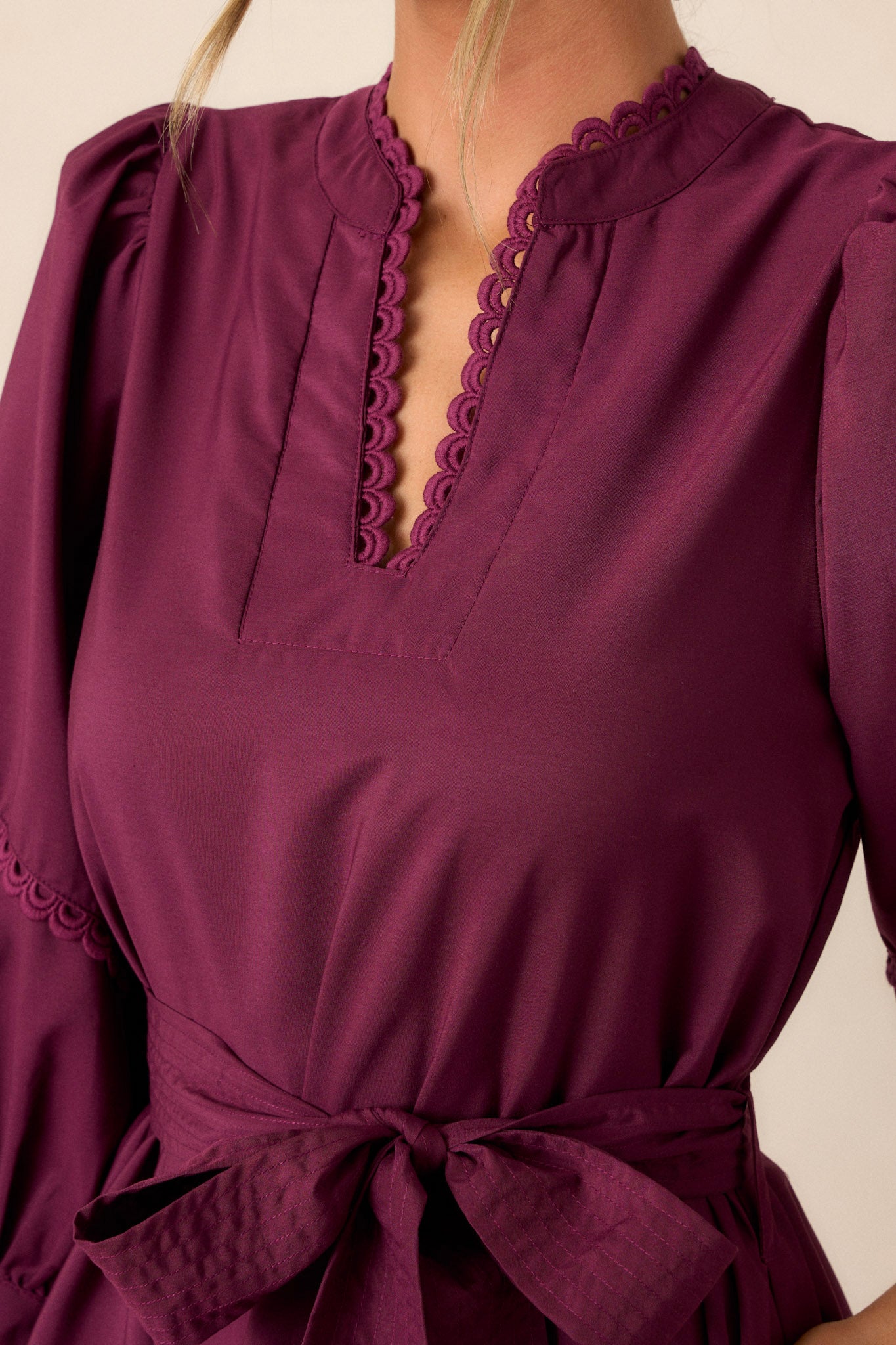 Close-up of the plum mini dress focusing on the split neckline with scalloped detailing, the self-tie drawstring belt, and the intricate scalloped edges on the tiered bishop sleeves.