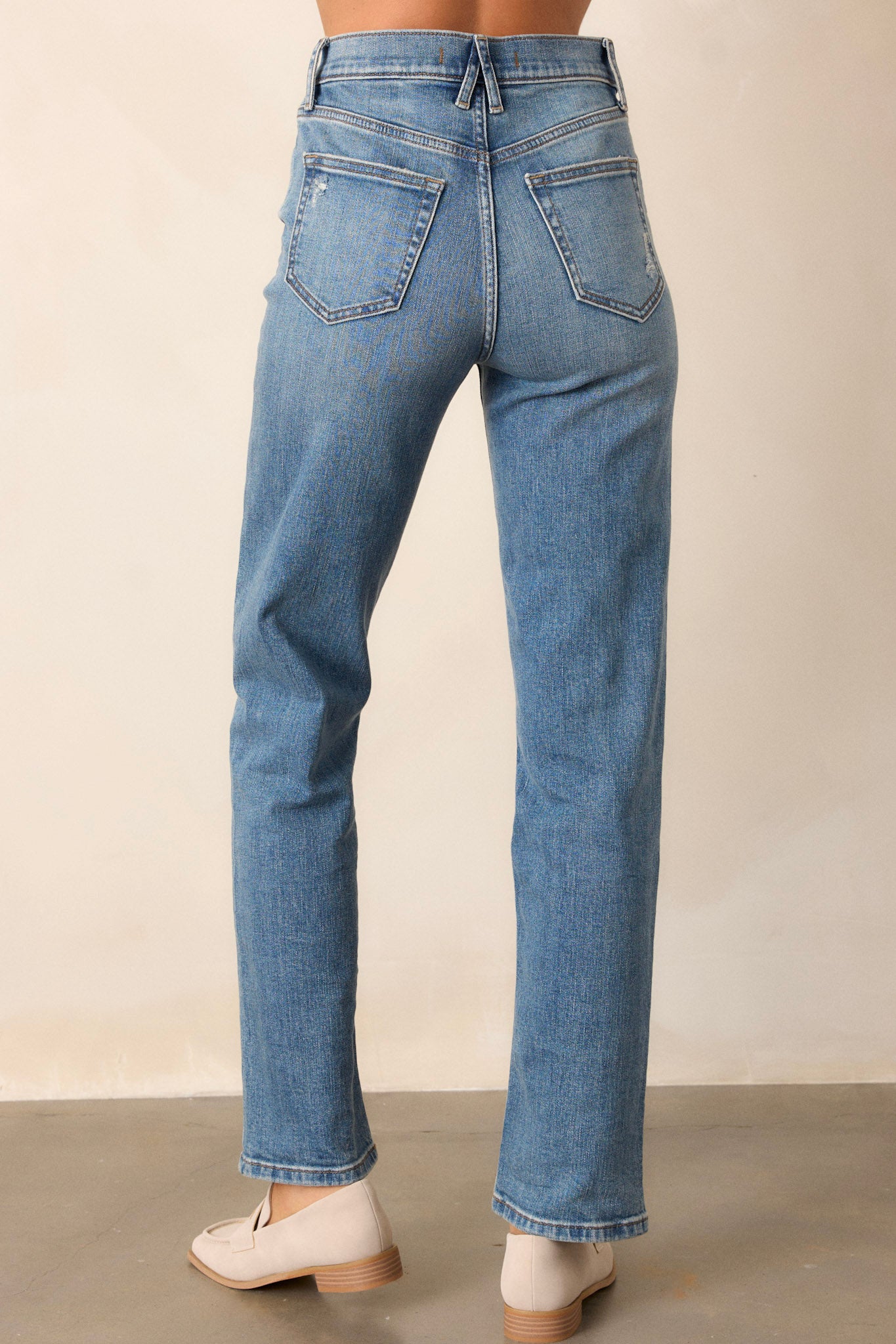 Back view of medium wash straight leg jeans featuring a high waist design, functional front & back pockets, distressed pocket detailing, a button & zipper closure, and a straight leg.