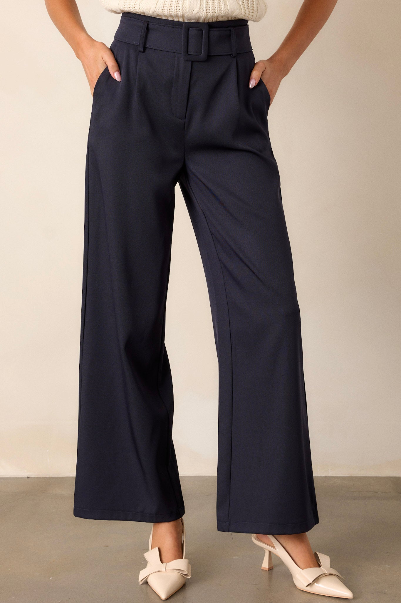 Front view of navy belted pants featuring a high waisted design, a hook and bar closure, a built-in adjustable cloth belt, functional pockets, and a wide leg.