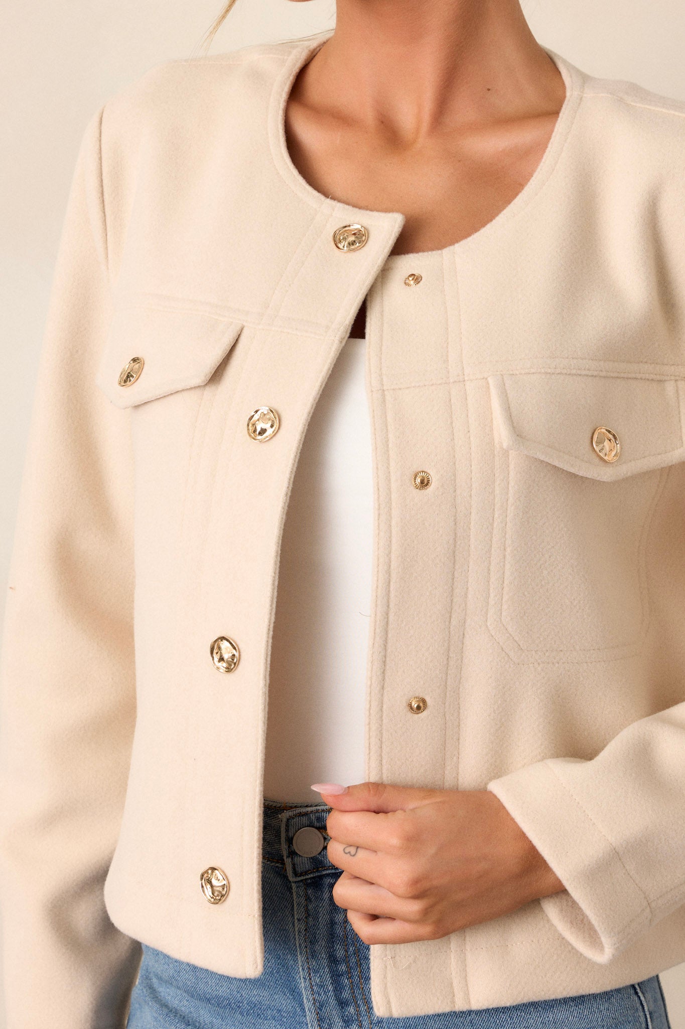 Close-up of this ivory jacket that features gold hardware, a scoop neck, two functional breast pockets, and a cozy tweed fabric.