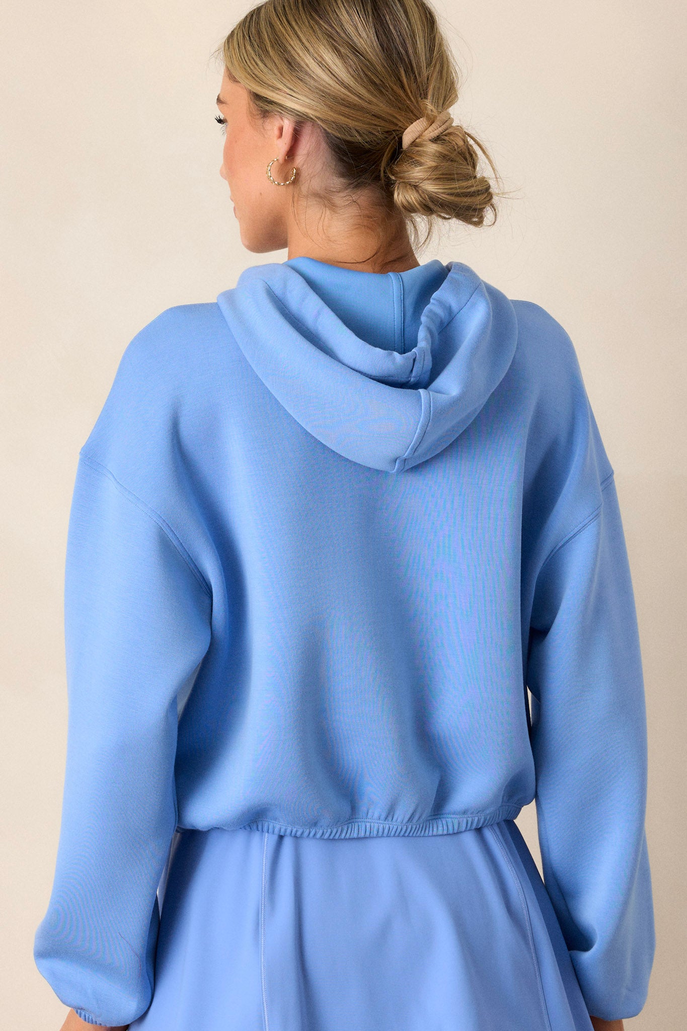 Back view of the cornflower blue hoodie emphasizing the slightly cropped design, elastic hem, and the finely knit fabric, showing the fit and overall structure from the back