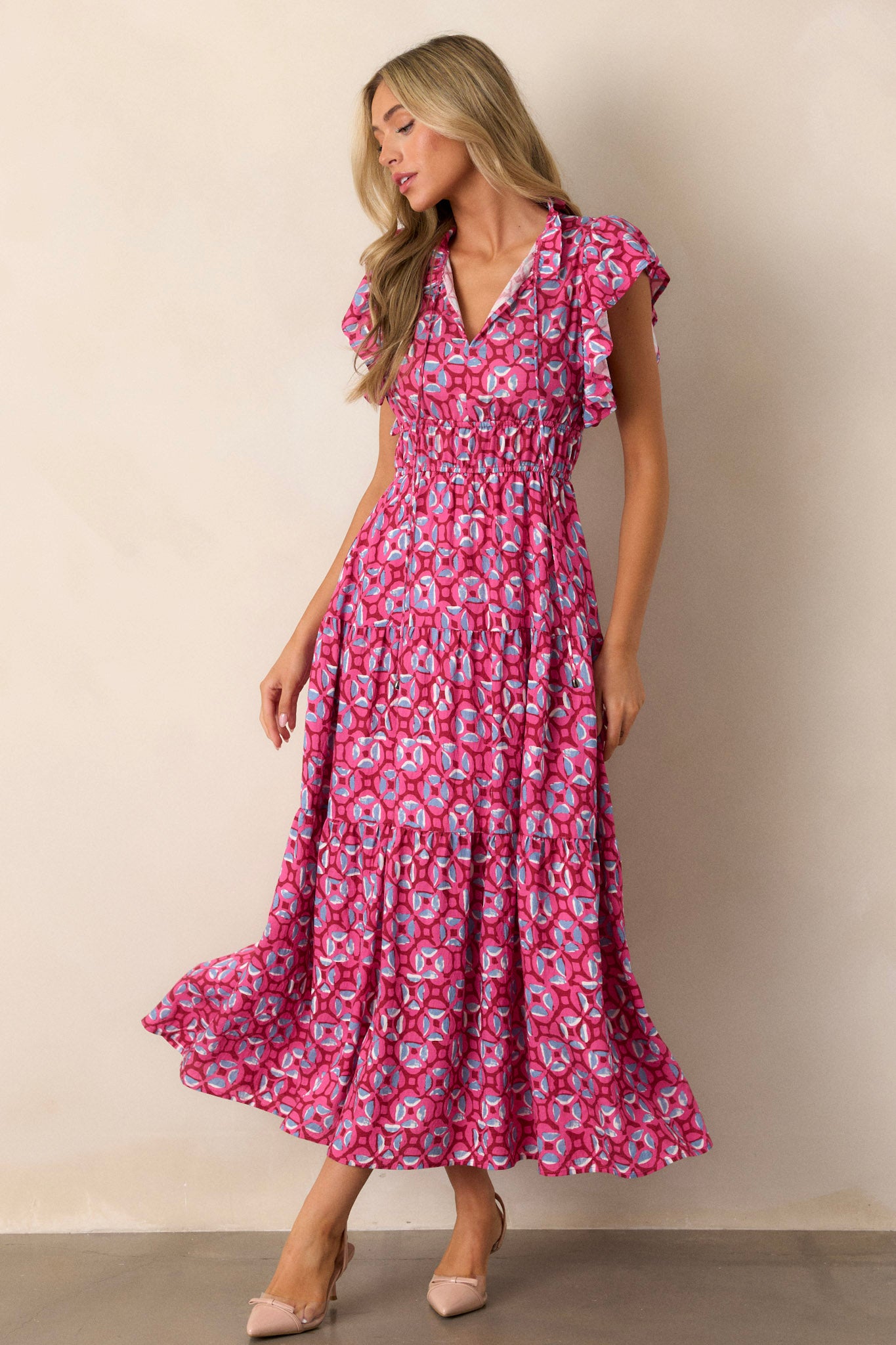 Full-length view of a model wearing the pink maxi dress, featuring the ruffled v-neckline, self-tie drawstring, elastic waistbands, functional hip pockets, tiered design, and short ruffle sleeves.