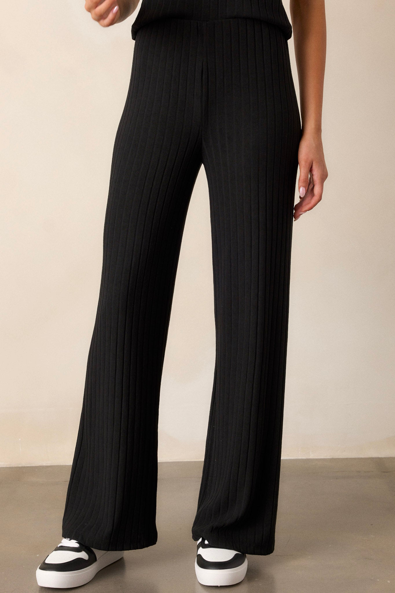 Full length view of the black pants featuring a high waisted design, a thick elastic waistband, ribbed fabric, and a straight leg cut.