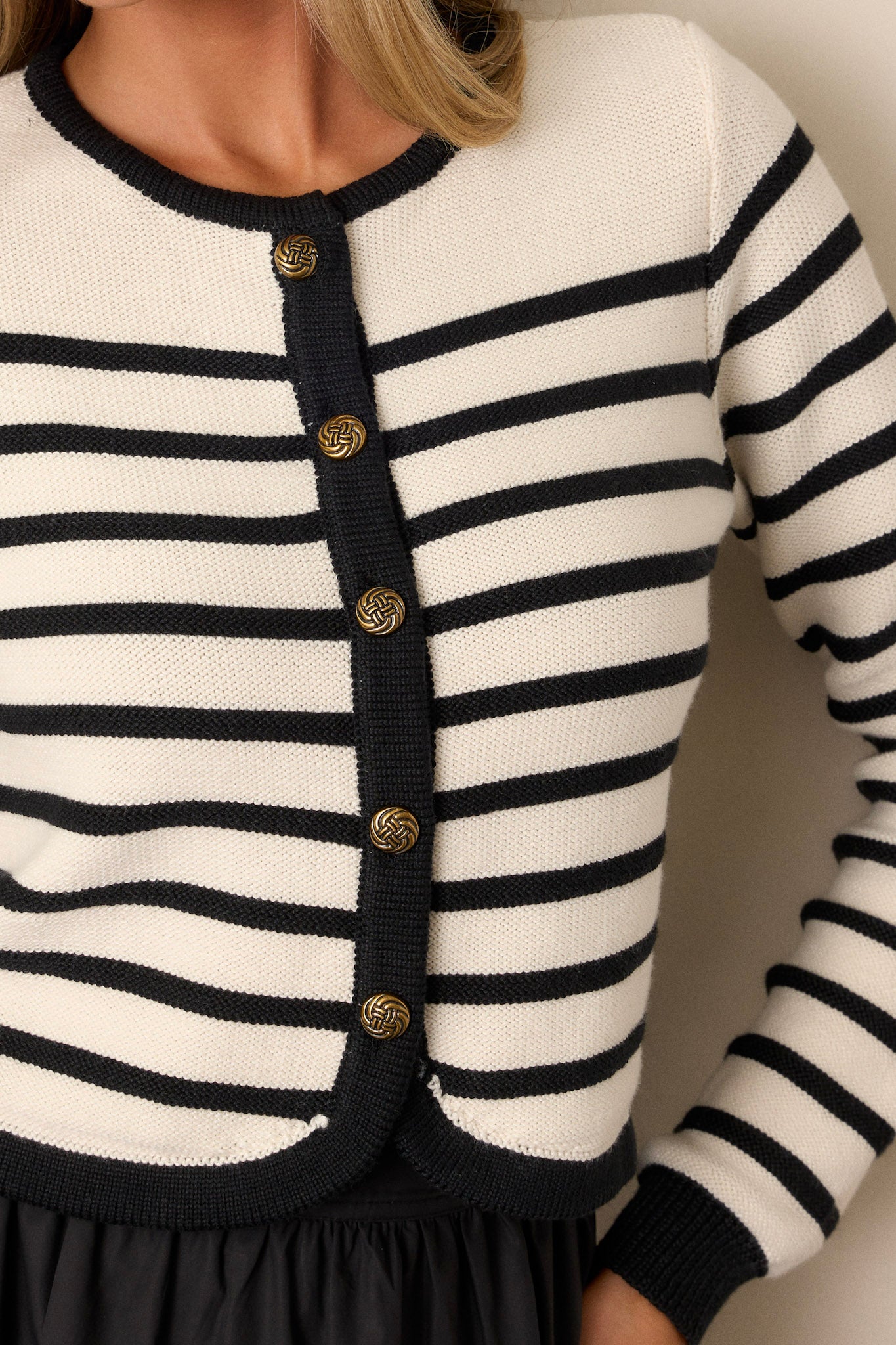 Close-up view of this ivory cardigan that features gold hardware with a functional button front, and a ribbed neckline and cuffs.