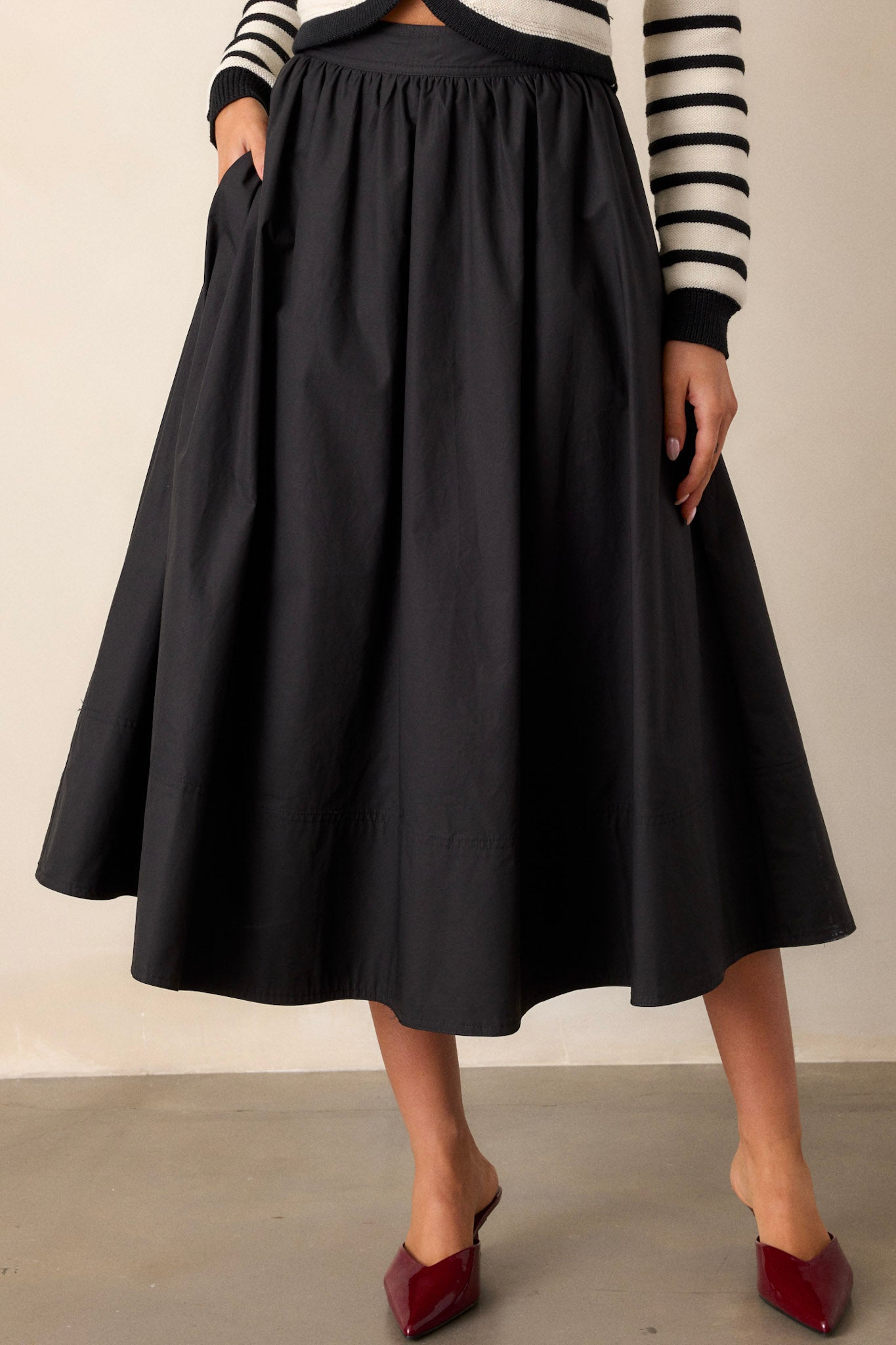 Close-up of the black 100% cotton midi skirt showing the high waisted design, discrete side zipper, and functional hip pockets.