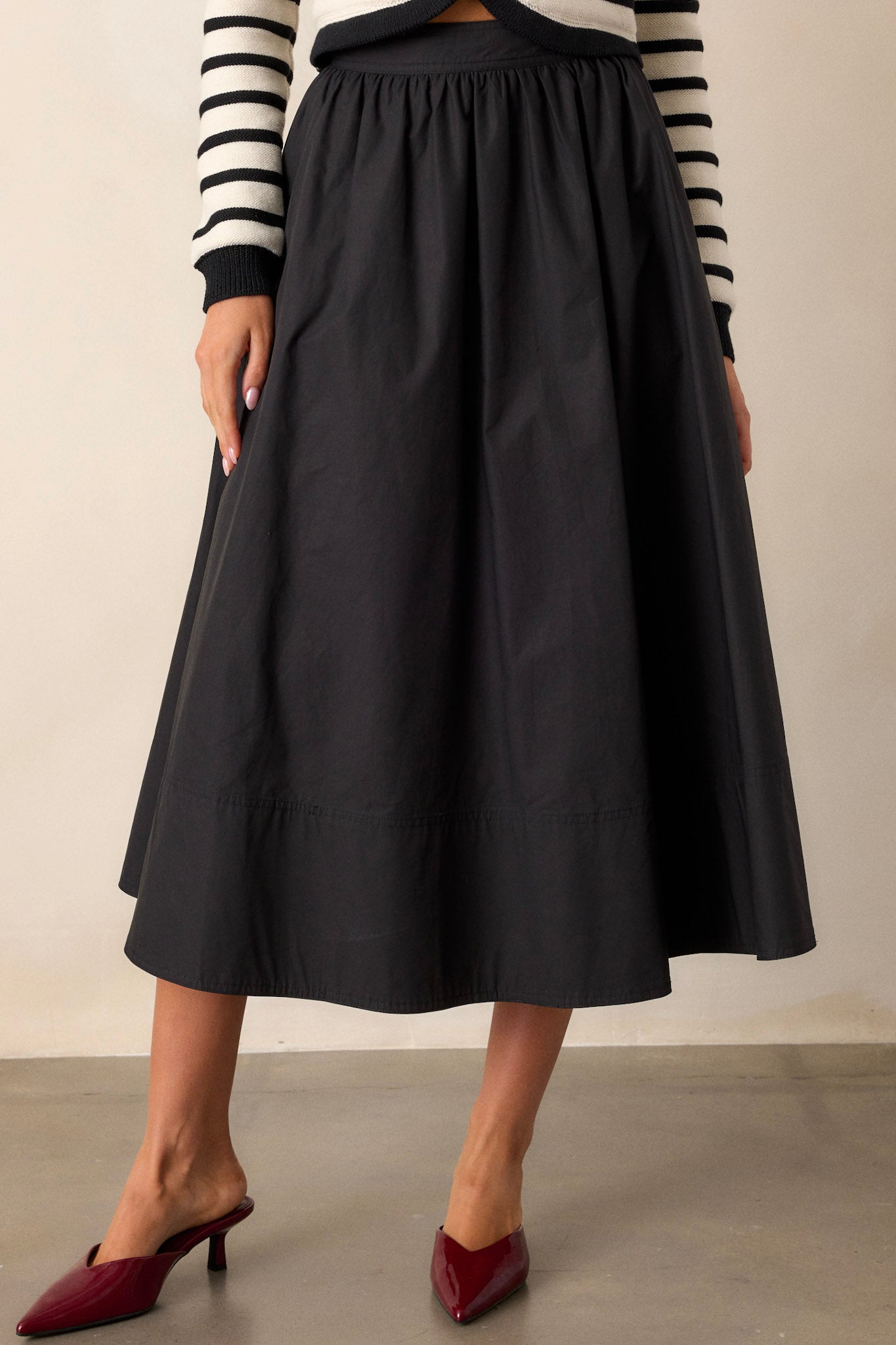 Front view of a black 100% cotton midi skirt featuring a high waisted design, functional hip pockets, and a thick hemline.