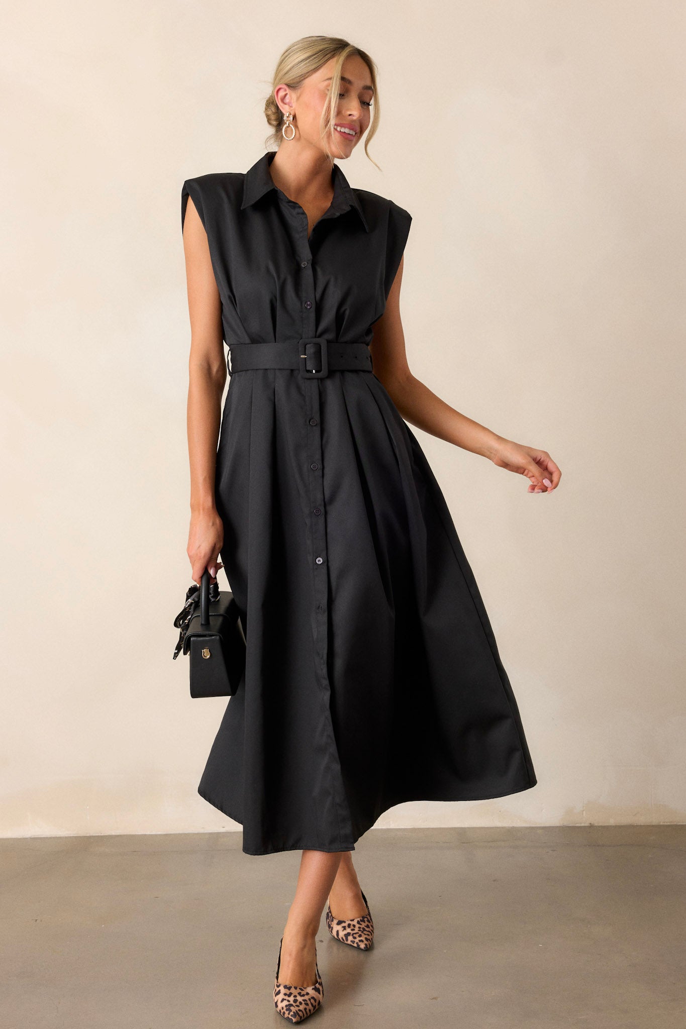 Movement view of this black dress that features built-in shoulder pads, a functional belt and a functional button front.