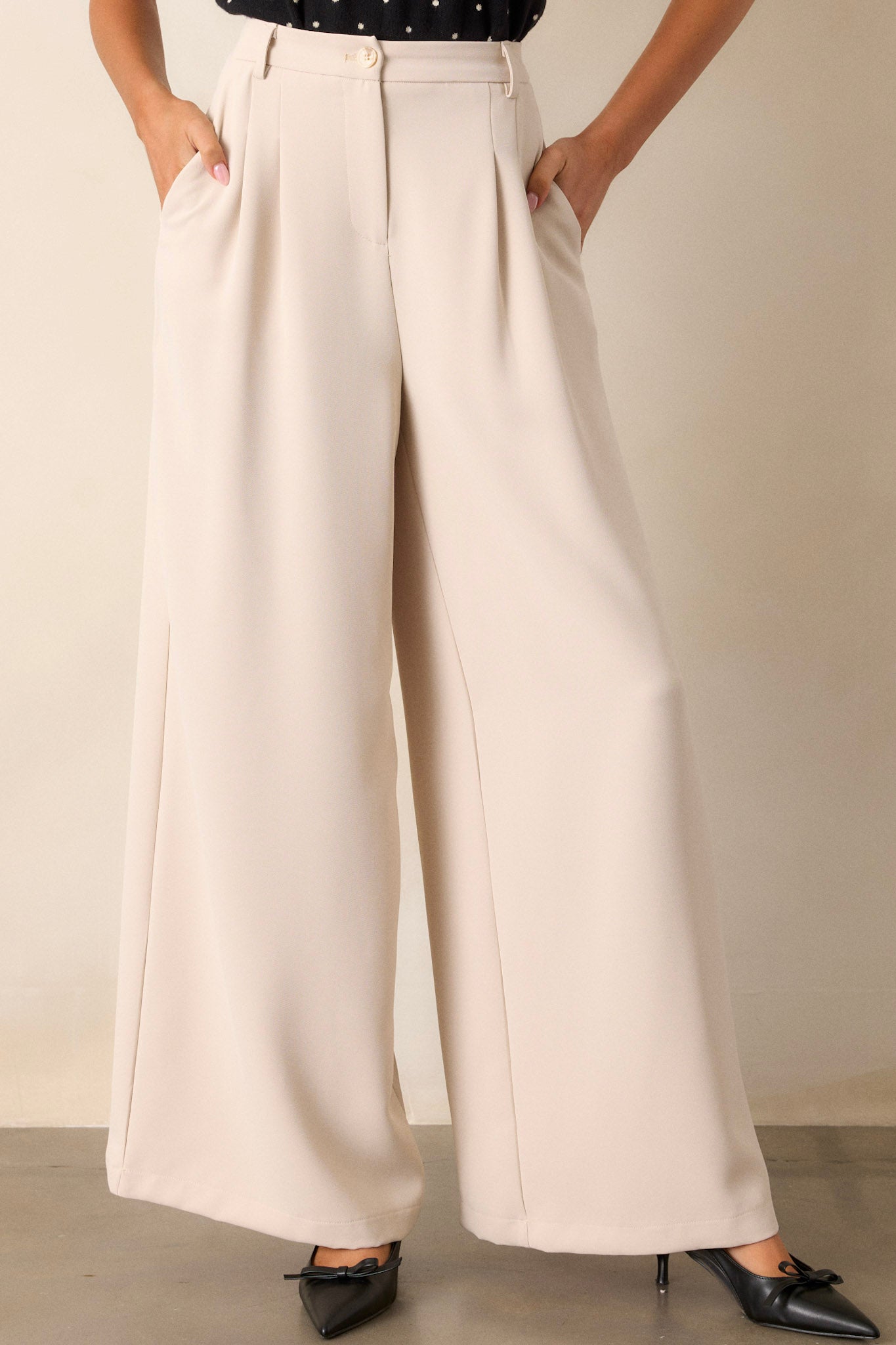 Front view of these light taupe pants that feature an elastic waist insert, functional belt loops, a button zipper closure, functional hip pockets, slight pleating on the hips and a wide leg.