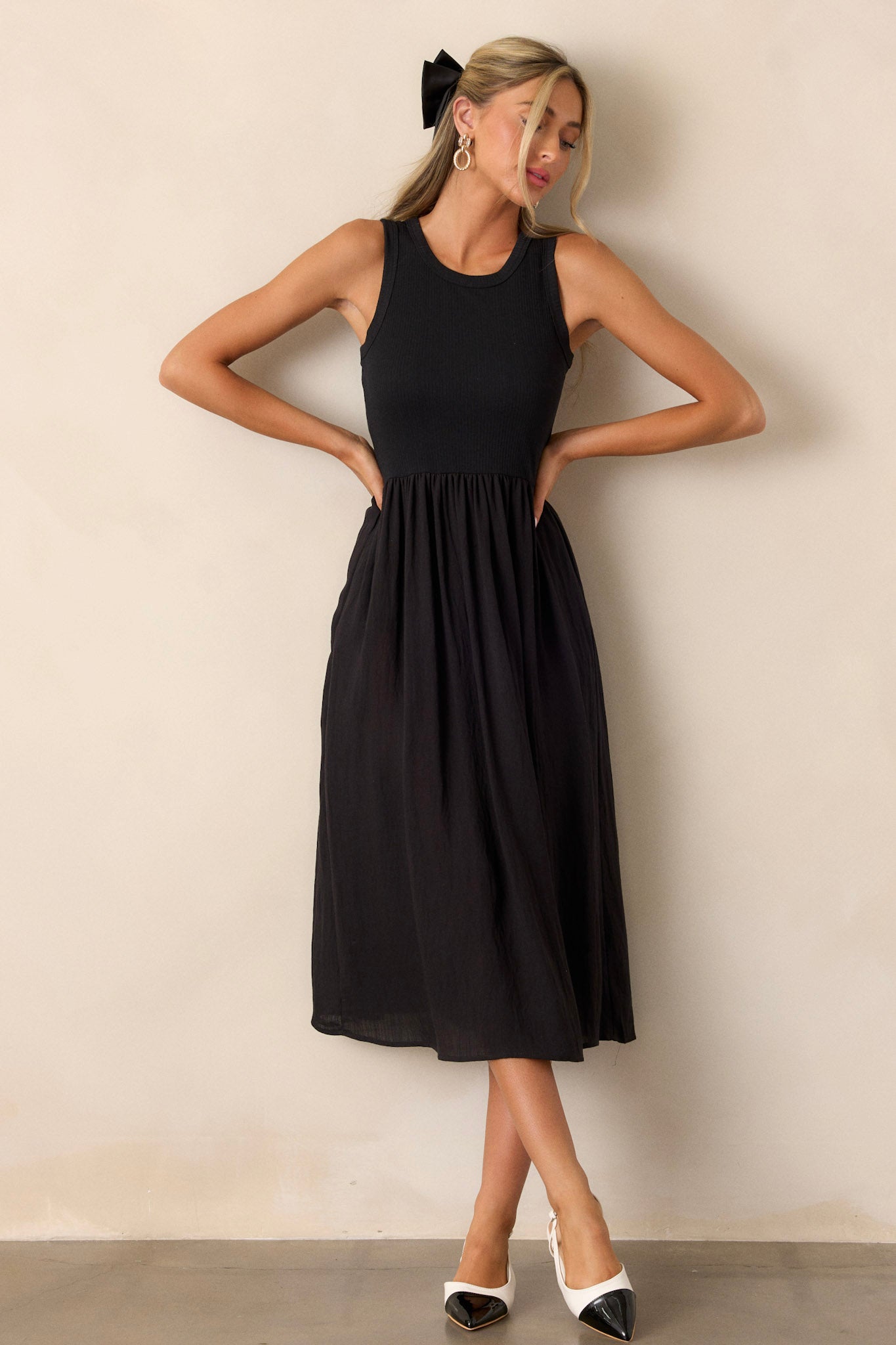 Full body view of this sleeveless black dress that features a crew neckline, a stretchy ribbed bust, a cinched waist, and flowing mid-length skirt.