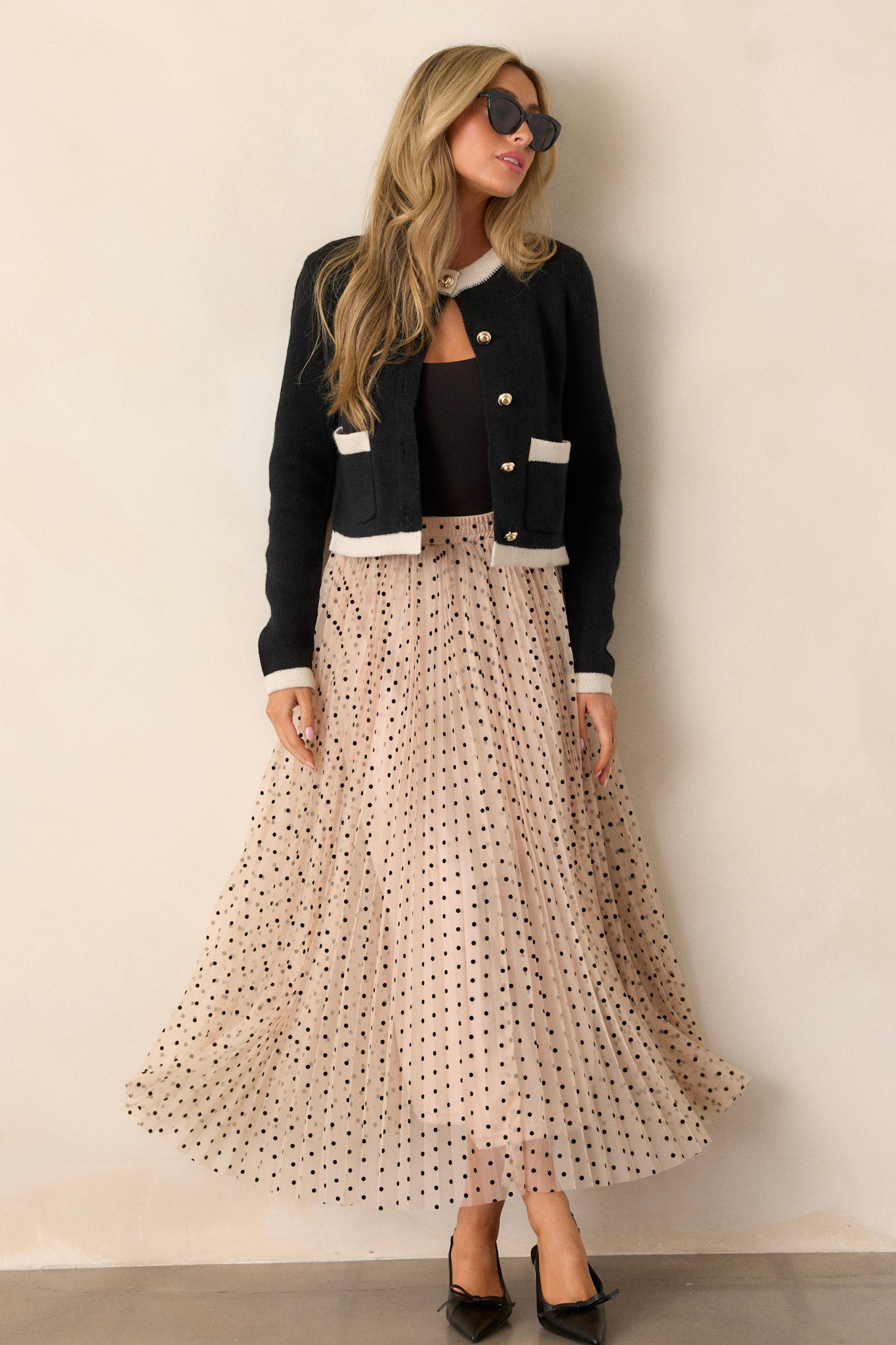 Full body view of this polka dot beige skirt featuring a high waisted design, an elastic waist band, a pleated design, and a flowing silhouette.