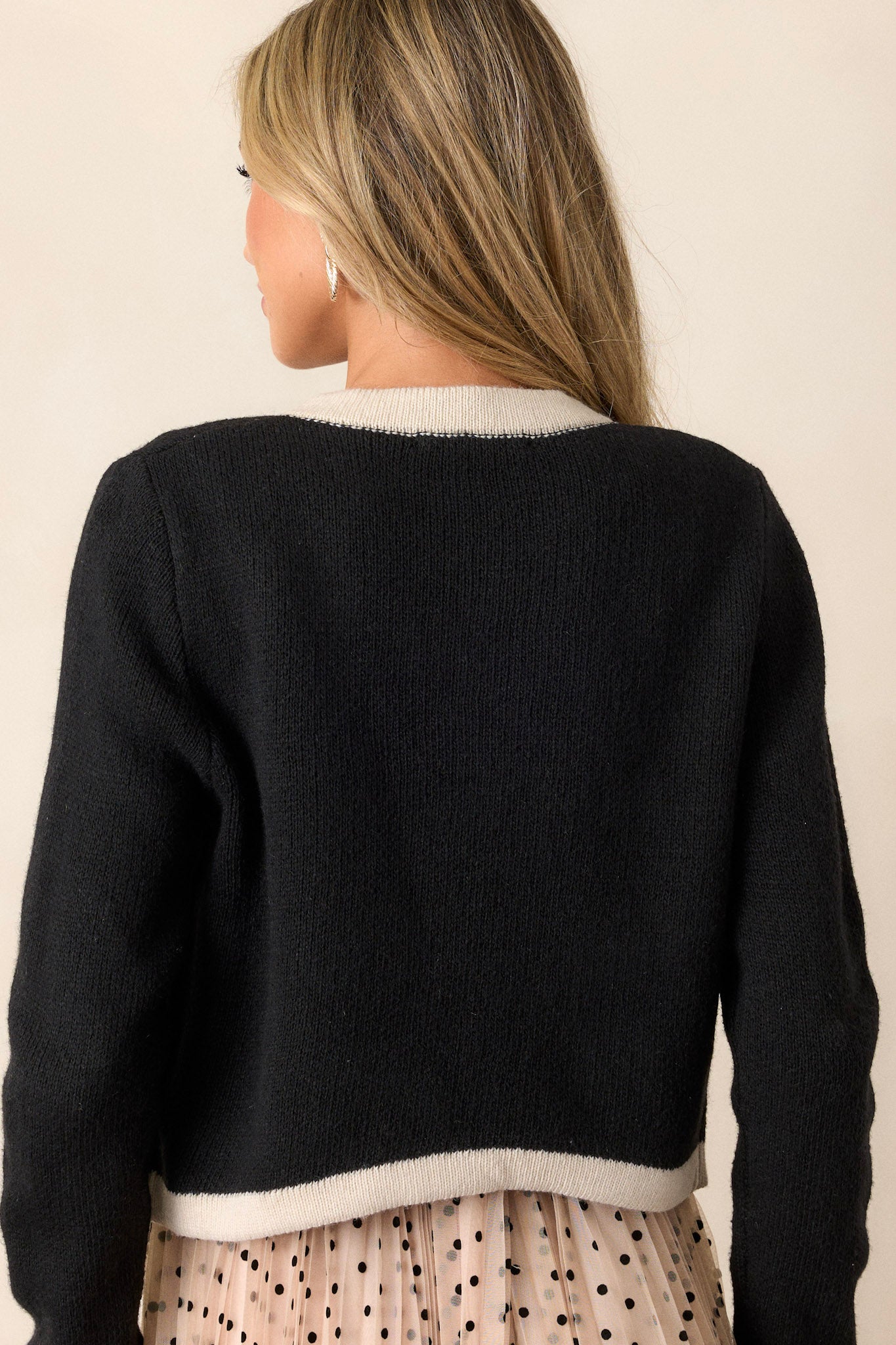 Back view of the black jacket highlighting the cream trim on the hem and sleeves, with the long sleeves and overall fit visible.