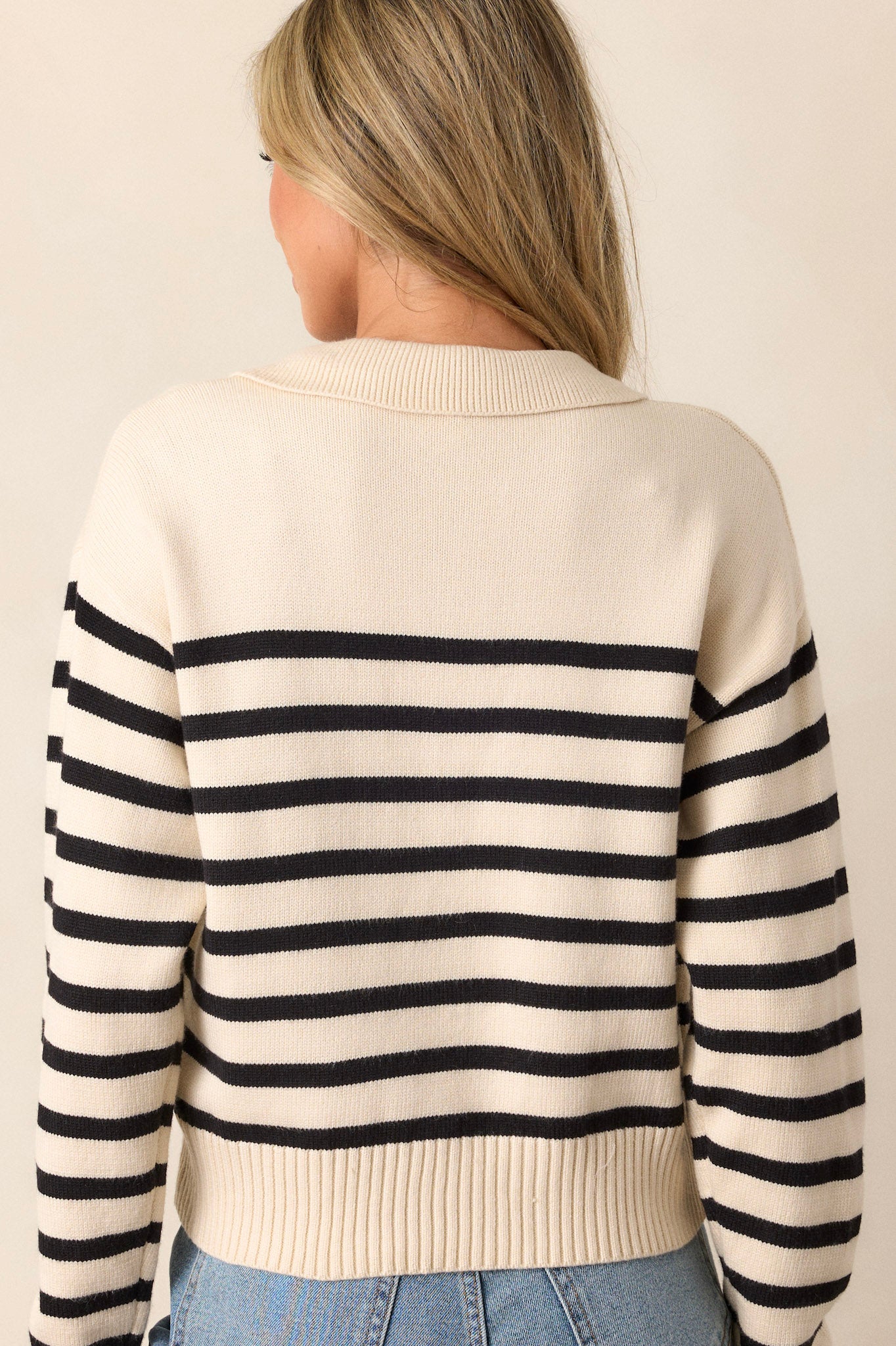 Back view of a beige sweater featuring a v-neckline with a collar, classic black horizontal stripes, long sleeves, and a ribbed hem and cuffs.