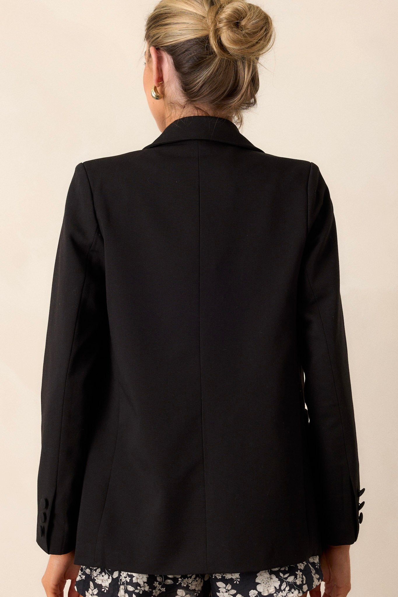 Back view of this black blazer that  features two functional pockets, functional buttons, a lapel collar, lightweight shoulder pads, and a multicolor print lining.