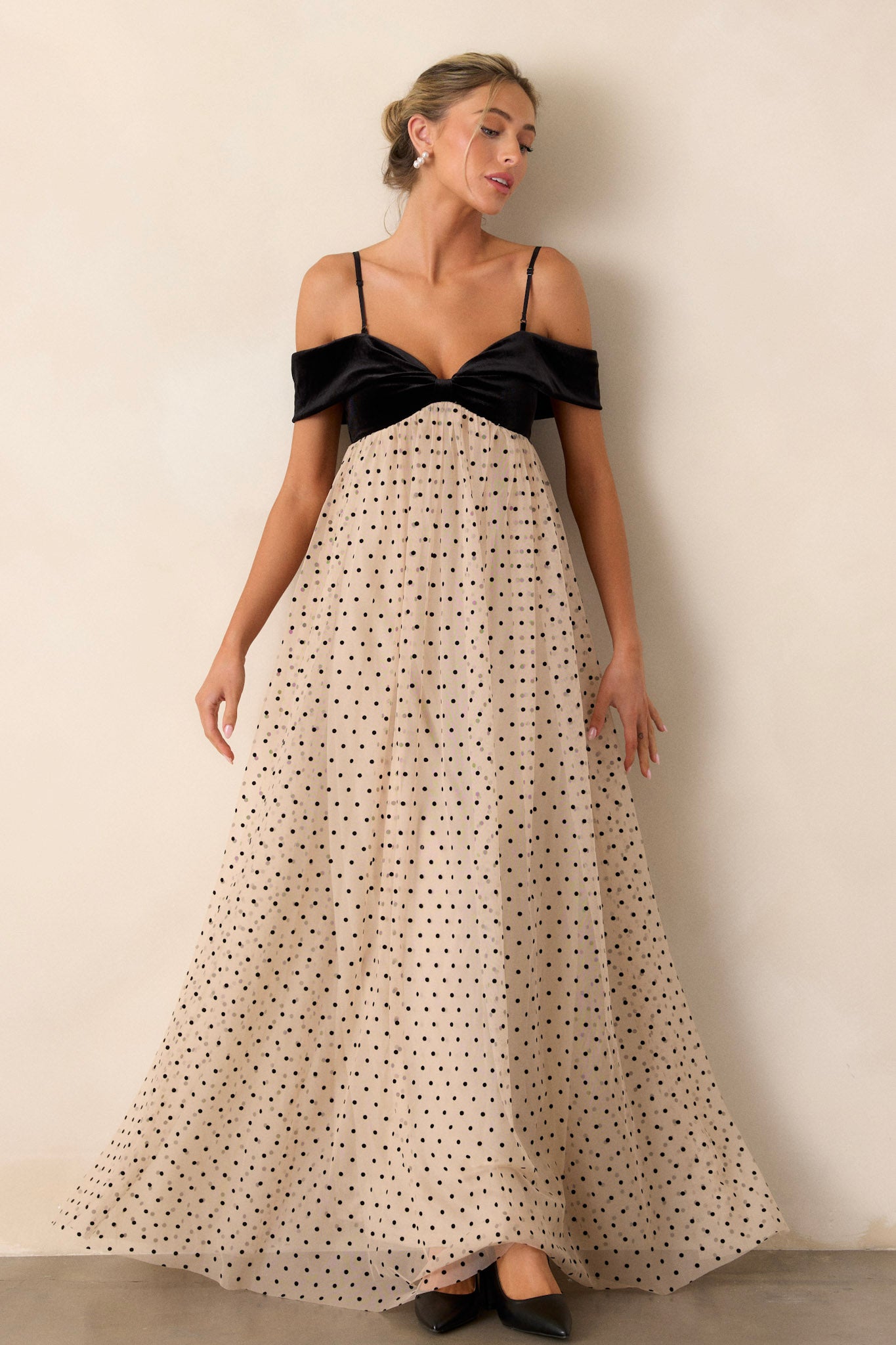 Front angled view of the dress featuring a velvet bust with a bow-shaped off-the-shoulder design, a flowy polka dot skirt, and a functional back zipper