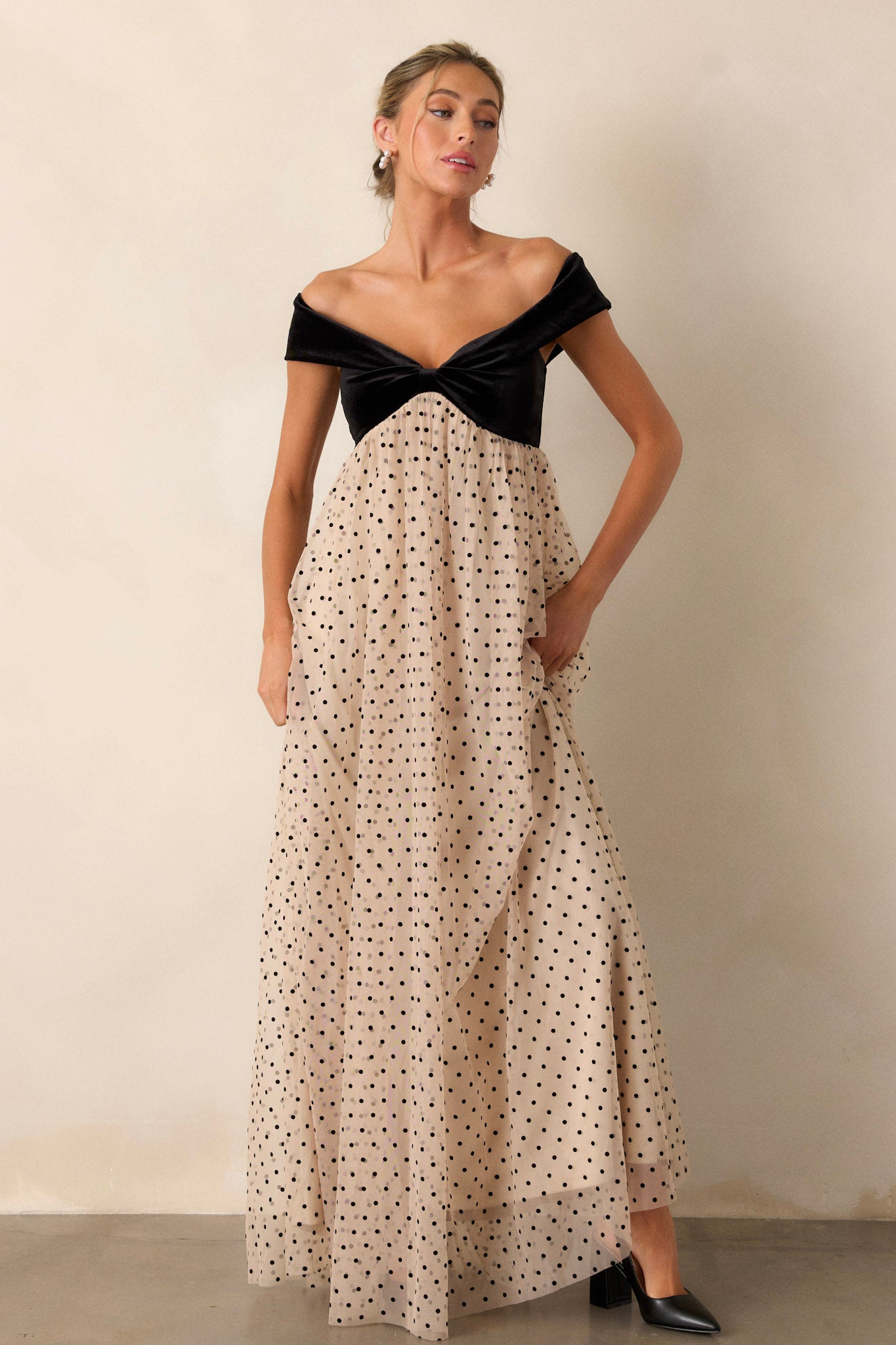 Front view of a dress featuring a velvet bust with a bow-shaped off-the-shoulder design, a flowy polka dot skirt, and a functional back zipper.