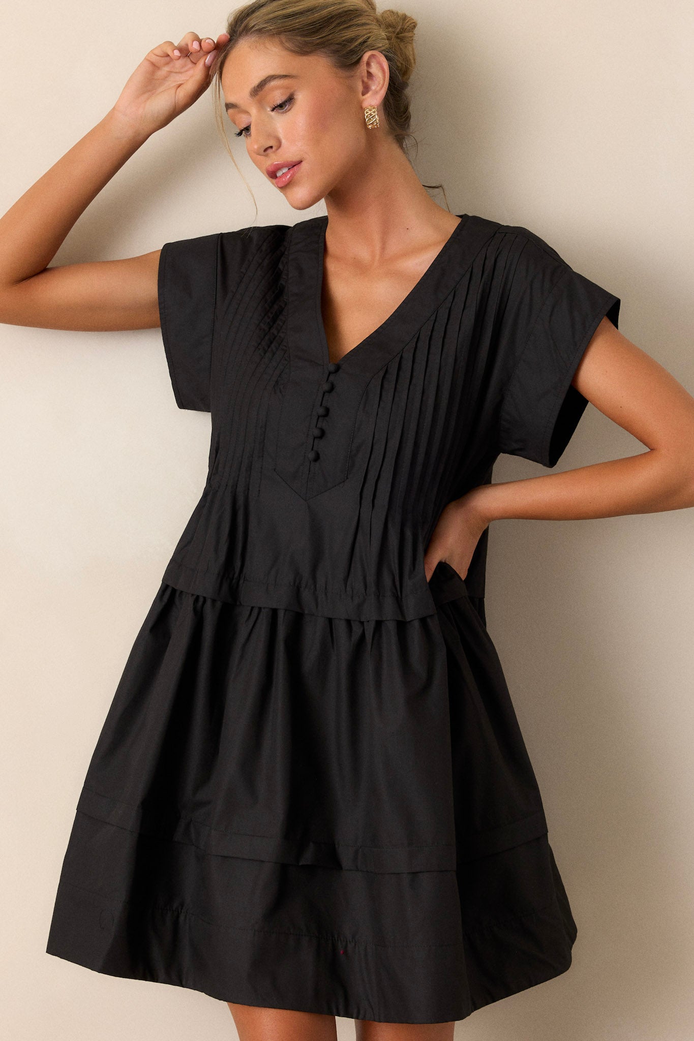 Angled view of the black dress displaying the deep V-neckline, button-front, and functional side pockets, giving a sense of the dress's fit and flow.