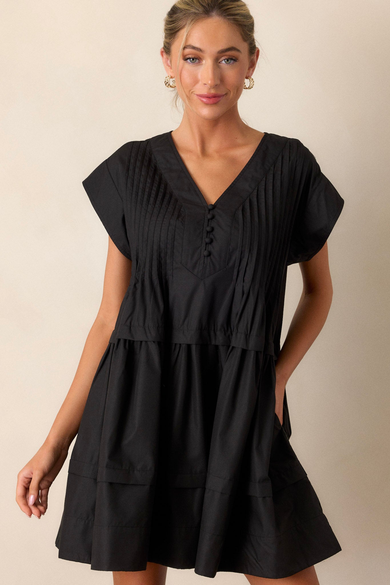 Front view of a black dress featuring a deep V-neckline, a functional button-front, and two functional side pockets