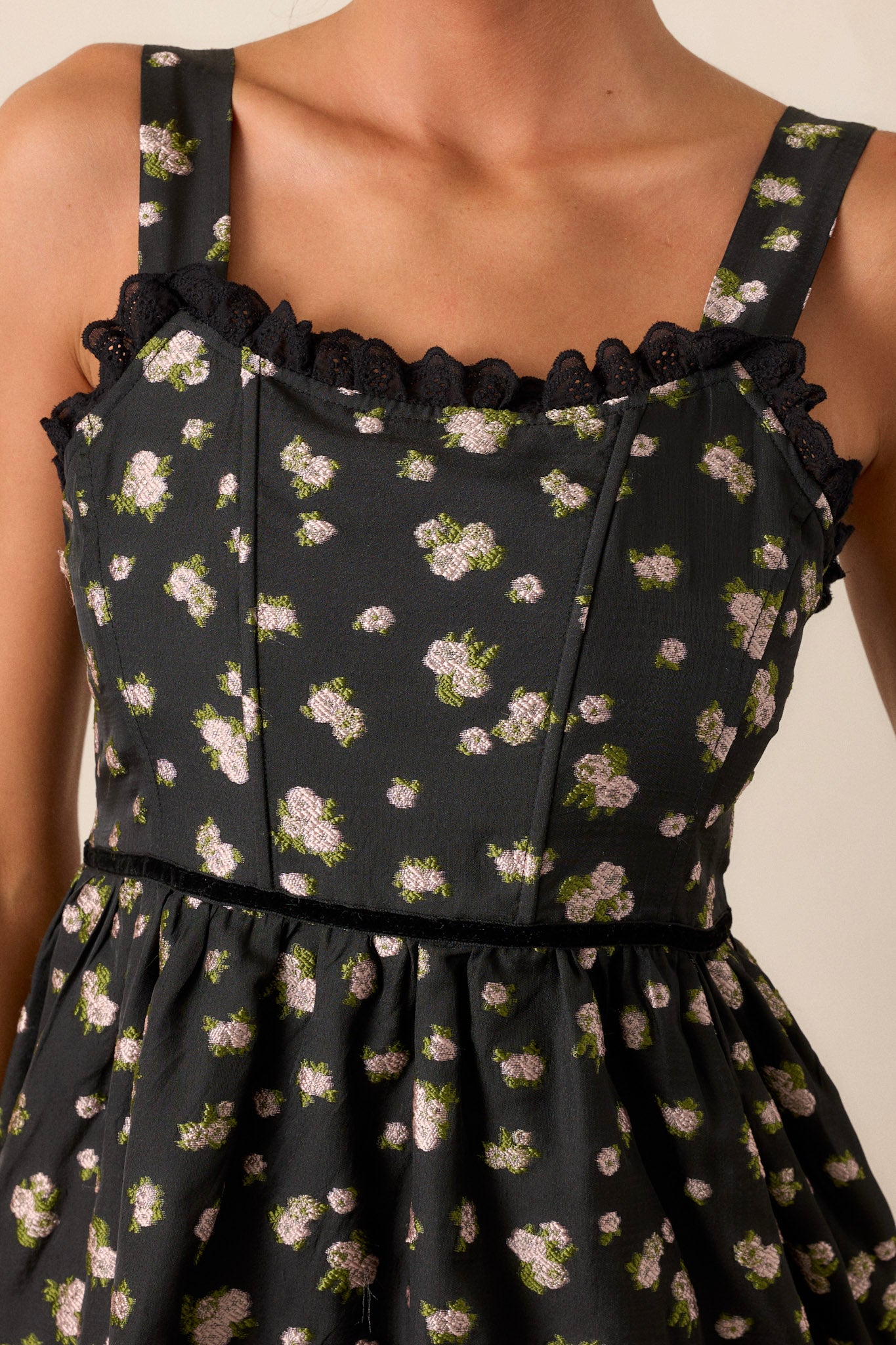 Close-up view of this black dress that features a back functional zipper, a corset style top, adjustable straps, a flowing skirt, an ivory floral print, and lace detailing.