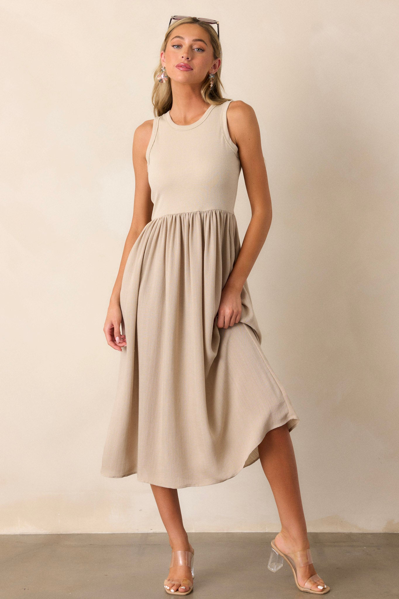 Front view of this sleeveless tan dress that features a crew neckline, a stretchy ribbed bust, a cinched waist, and flowing mid-length skirt.