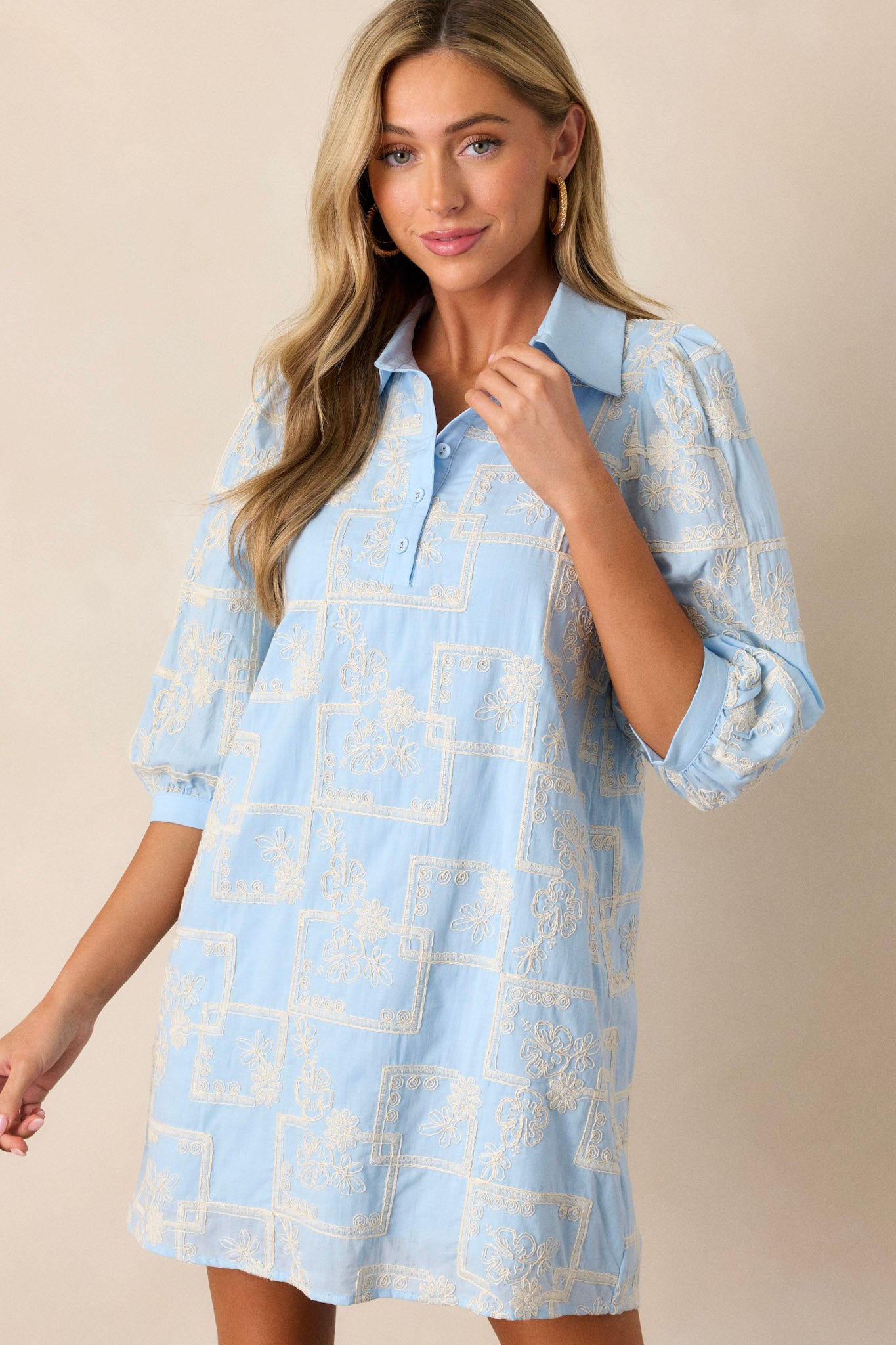 Front angled view of this dress that features a collared neckline, a functional button up bust, a white embroidered floral and square pattern, a relaxed fit and puffed half sleeves.