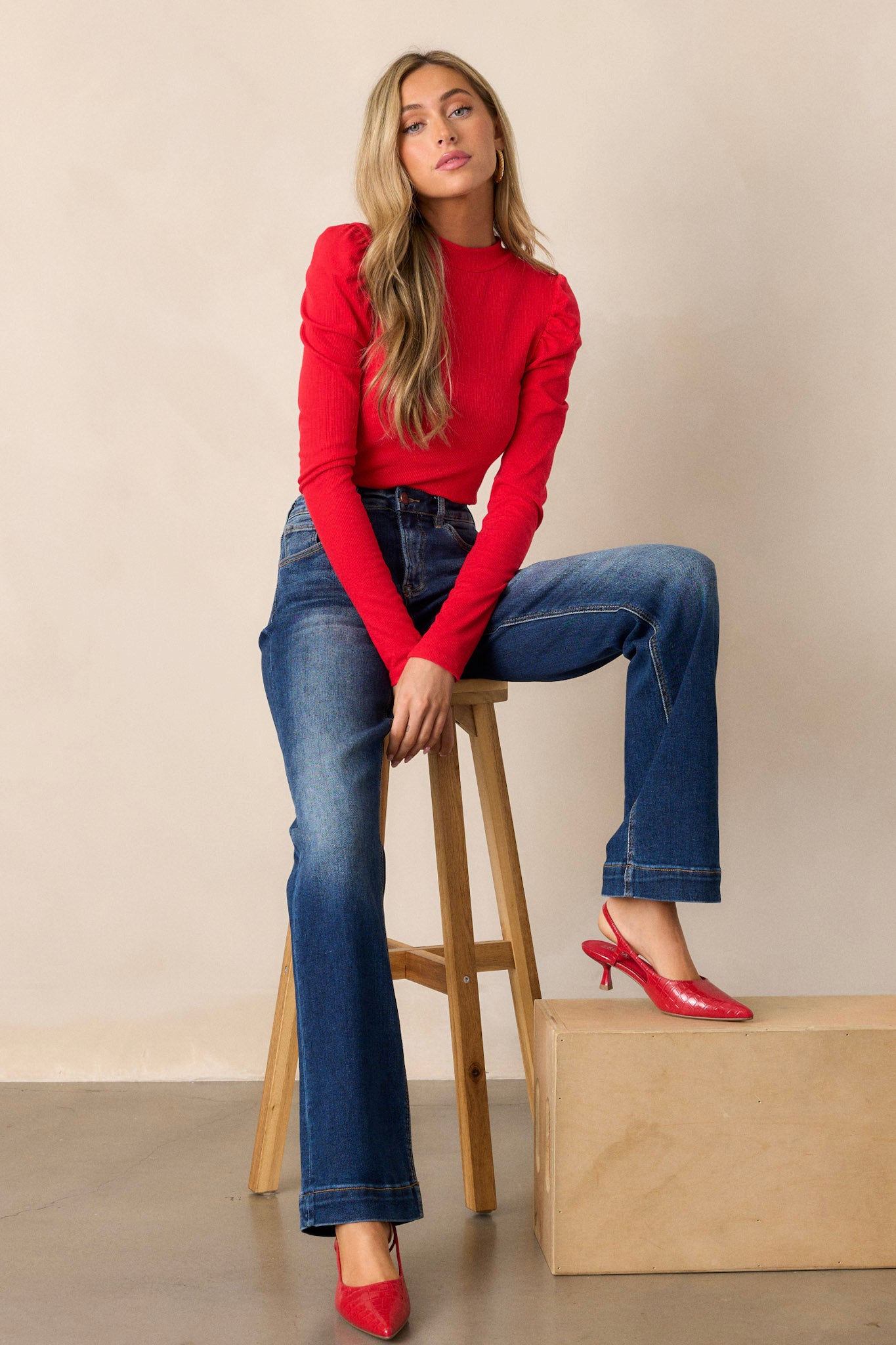 Full body view of a long sleeve ribbed top with a high neckline, a back cut-out with a loop closure, a soft ribbed material, and slight ruffled long sleeves.