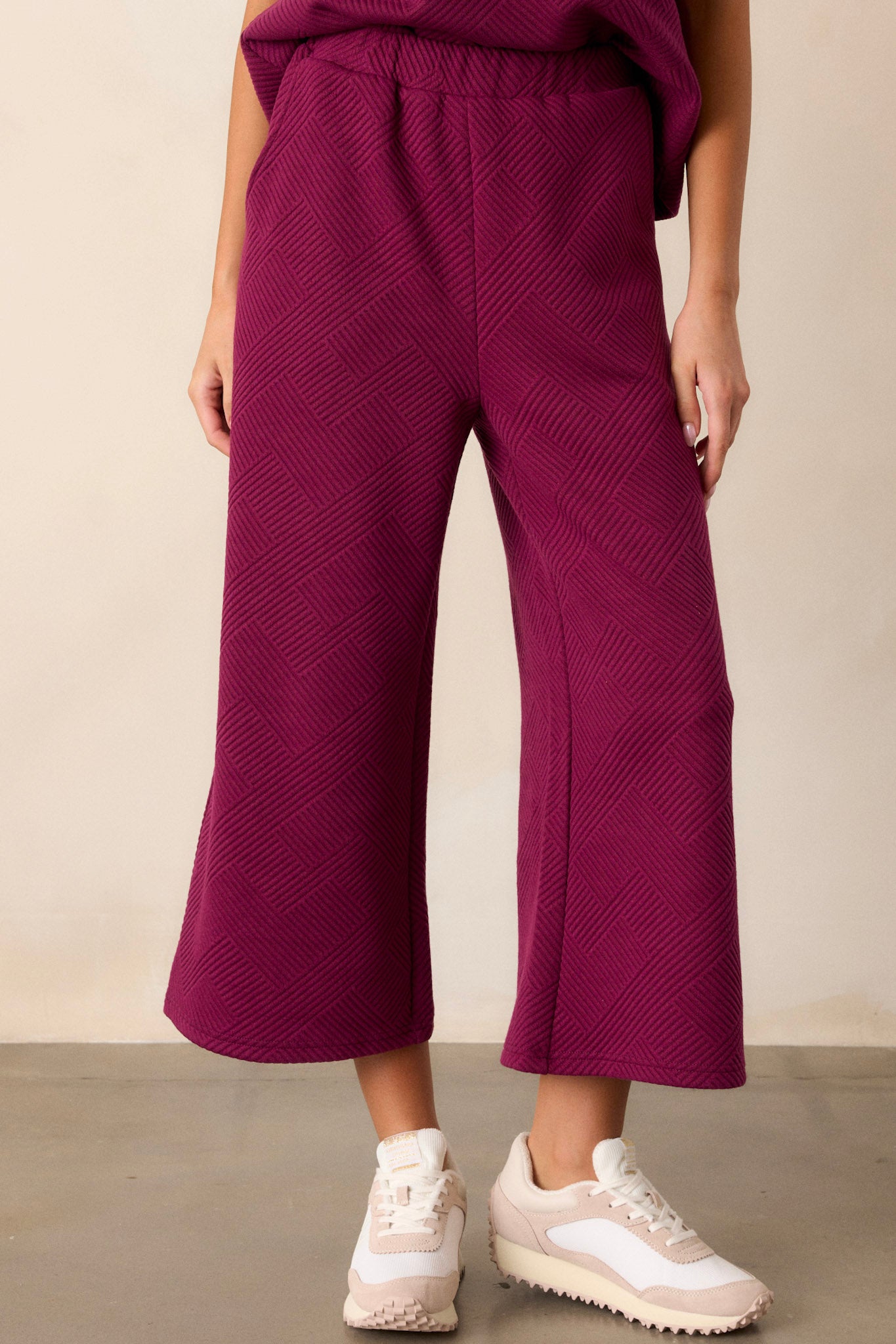 Front angled view of sangria purple pants featuring a high waisted design, an elastic waistband, functional hip pockets, a textured crisscross design, and a wide leg