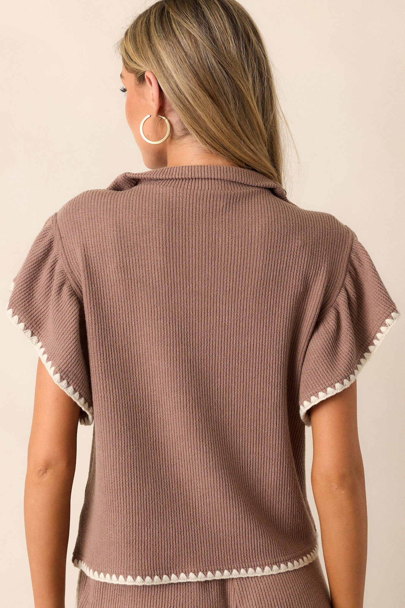 Back view of this mocha top that features a collared neckline, a quarter zip bust, a relaxed fit, a soft stitched material, a white ruffle trim and short cap sleeves.