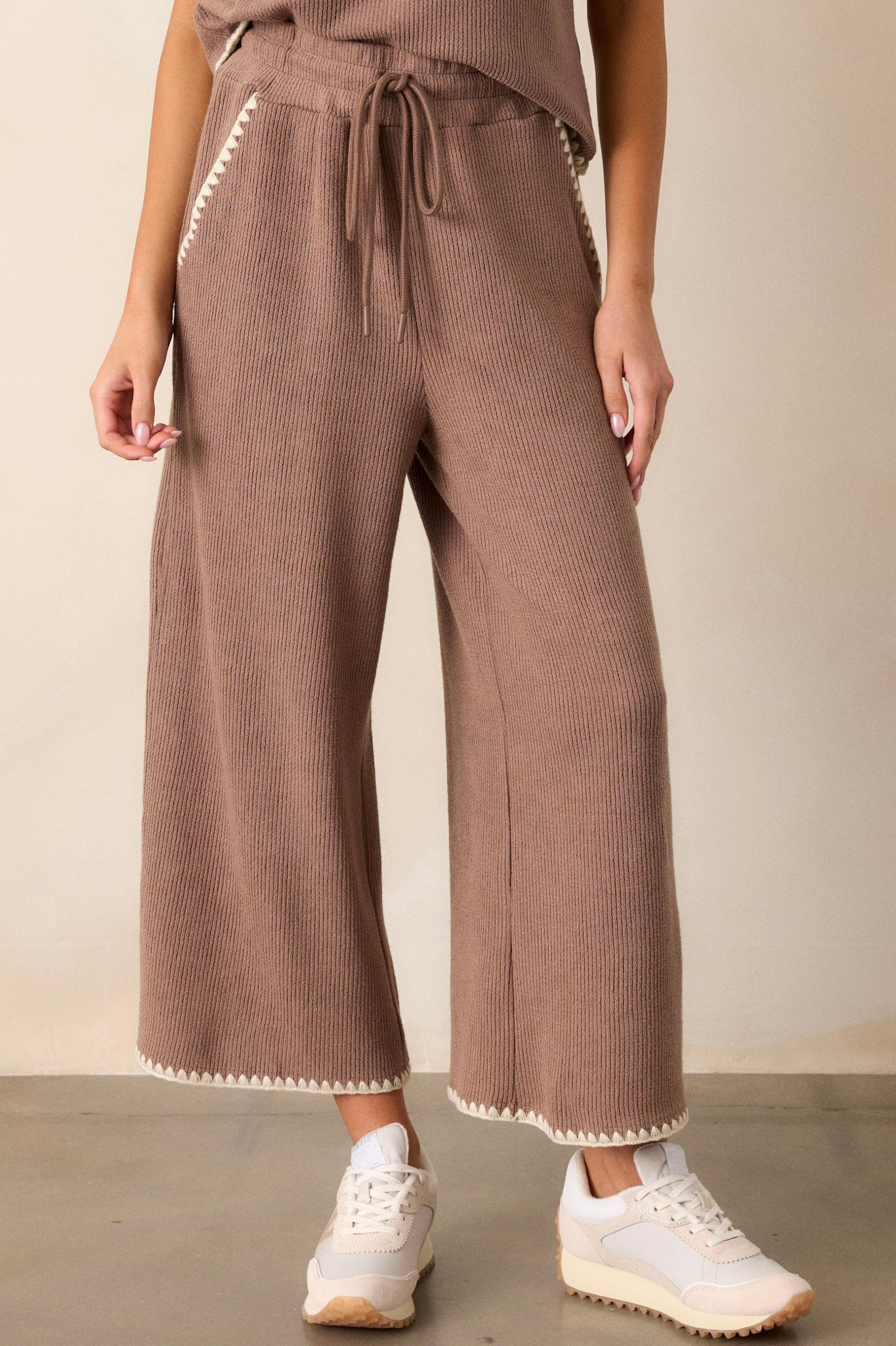 Close-up of these mocha pants that feature an elastic waistband, an optional waist drawstring, an ivory ruffle trim, functional hip pockets, a soft stitched material and a wide leg