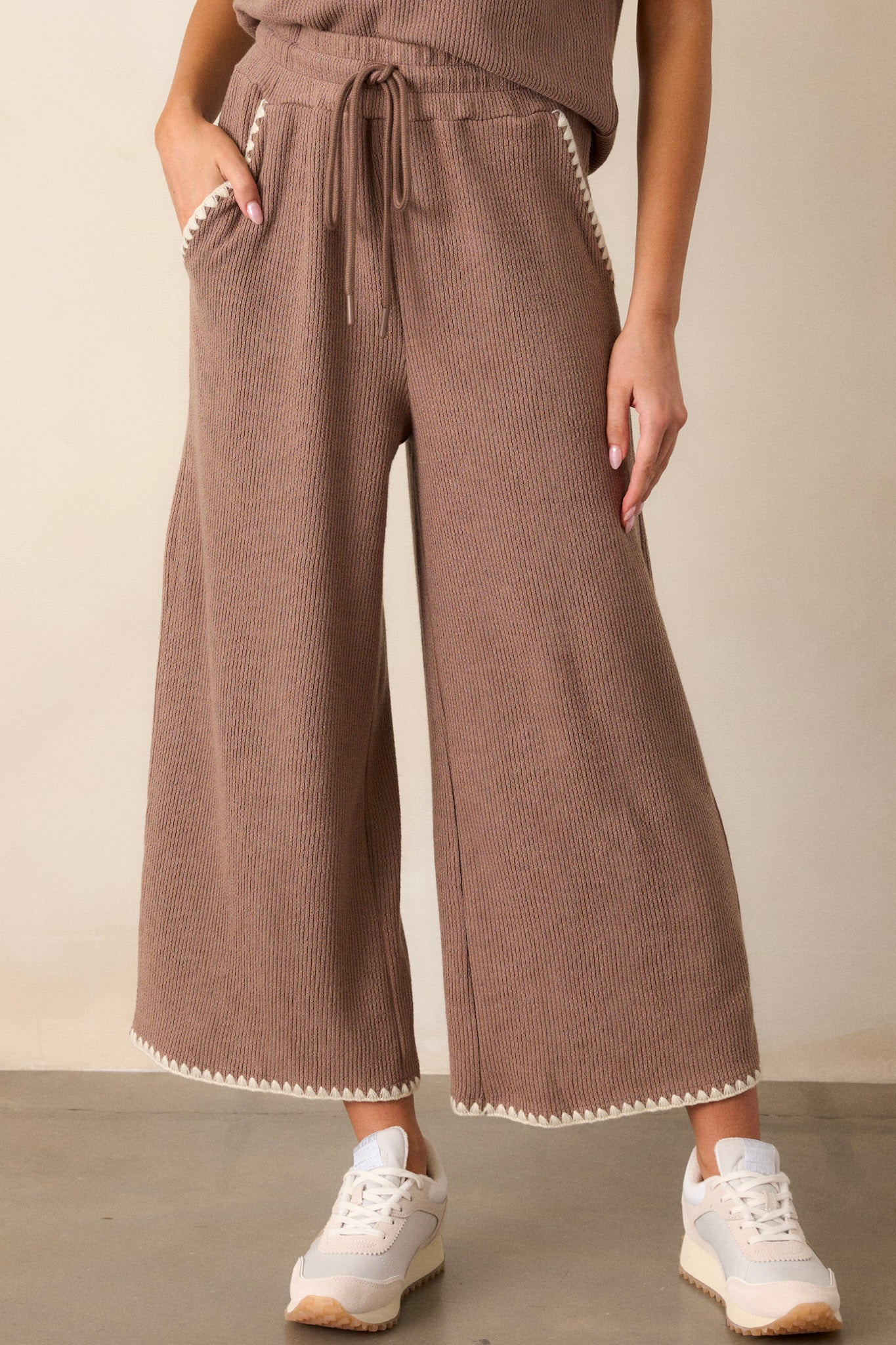 Front view of these mocha pants that feature an elastic waistband, an optional waist drawstring, an ivory ruffle trim, functional hip pockets, a soft stitched material and a wide leg