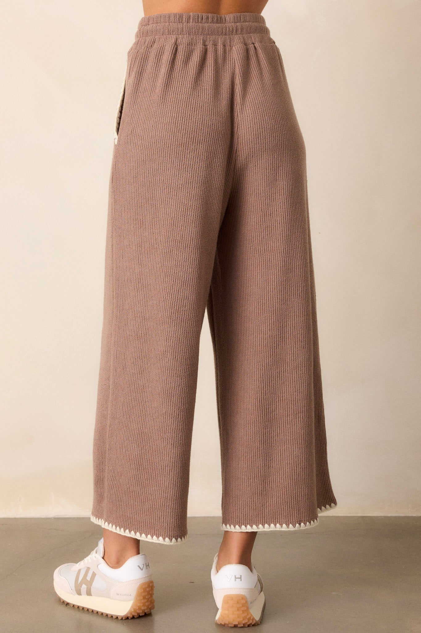 Back of these mocha pants that feature an elastic waistband, an optional waist drawstring, an ivory ruffle trim, functional hip pockets, a soft stitched material and a wide leg