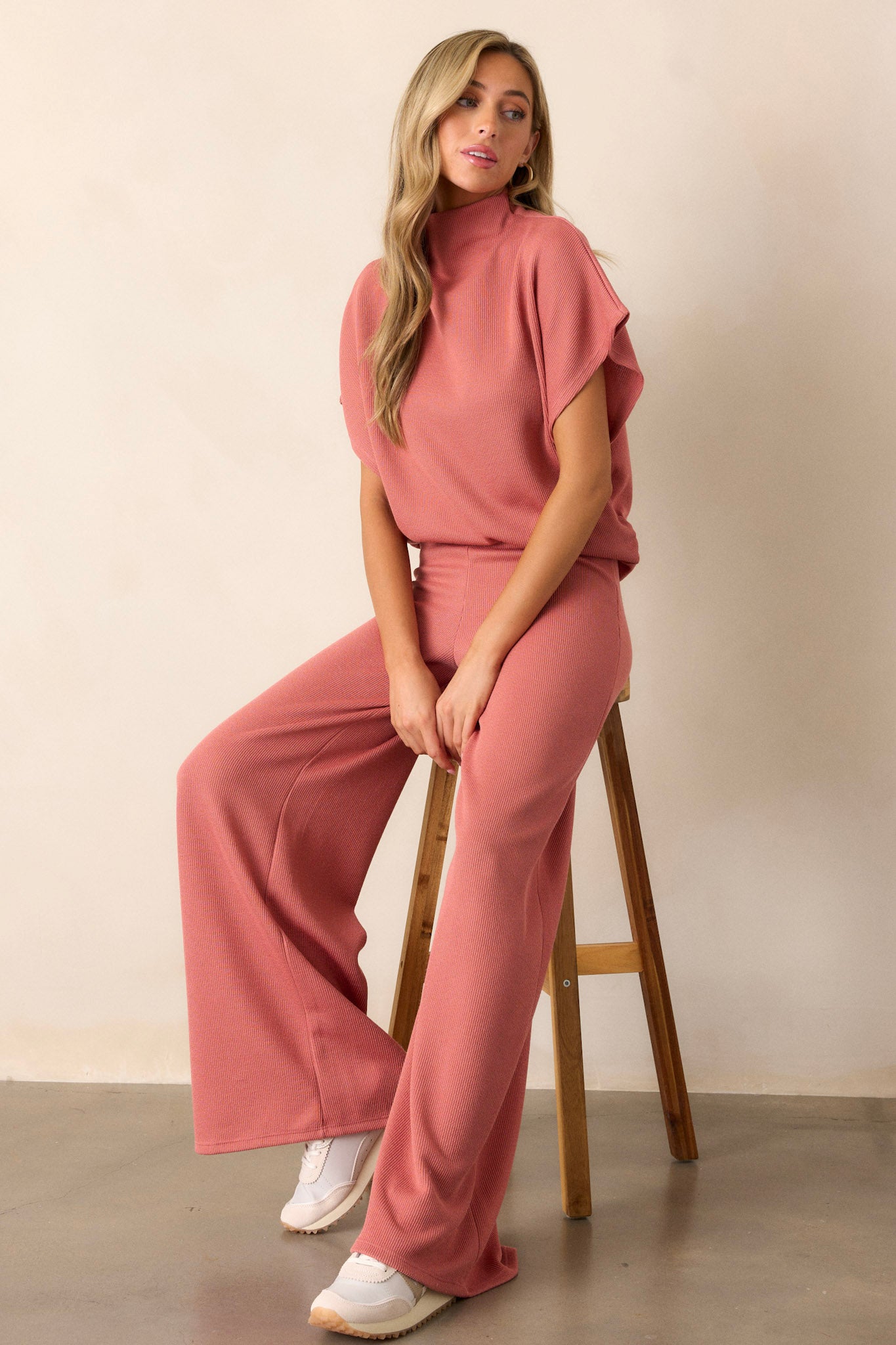 Seated view of this coral top that features a turtleneck, a knit towel like texture on the outside, a soft smooth inside, cinching in the hips and short flowy sleeves.